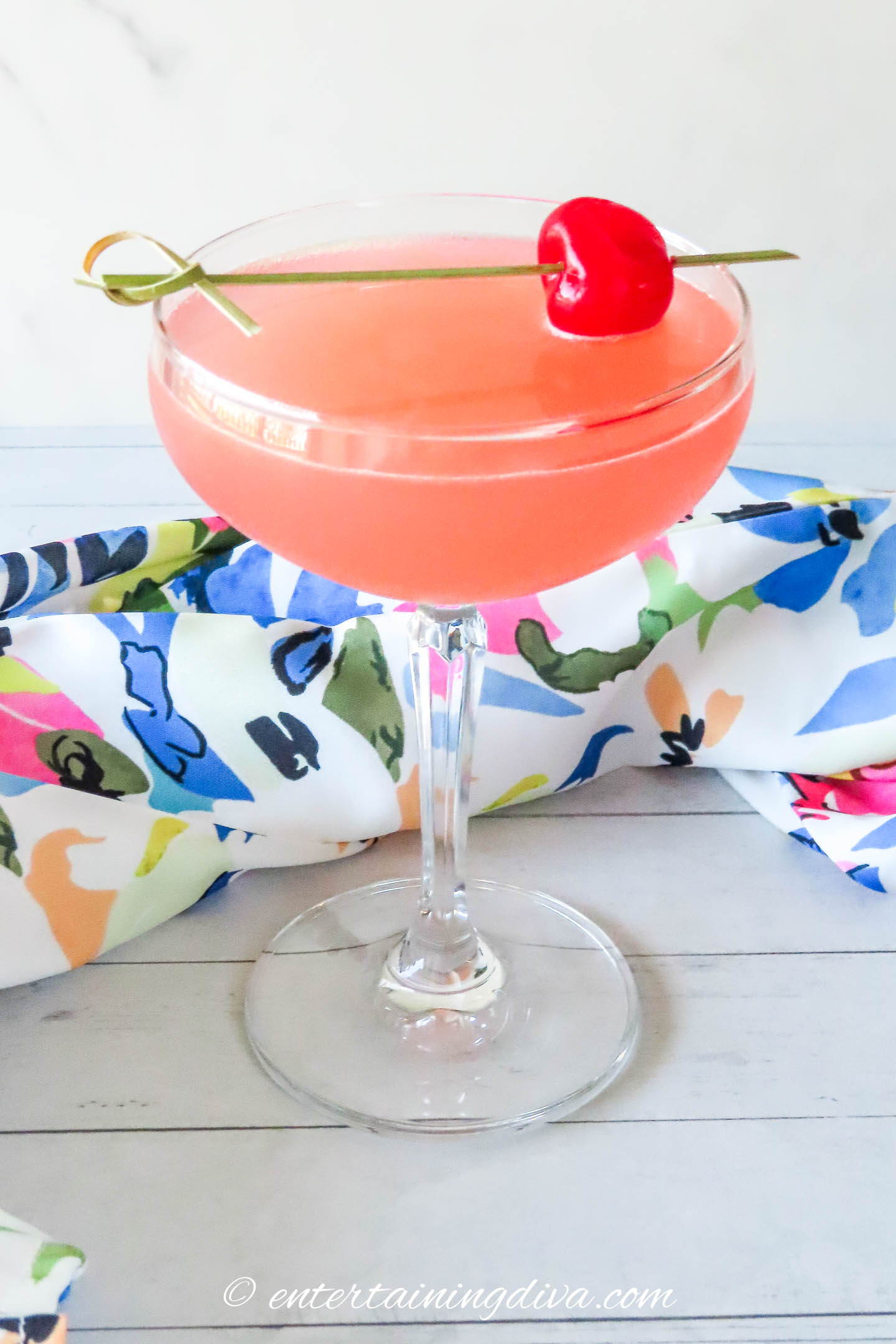 Azalea cocktail in a coupe glass with a maraschino cherry on a cocktail pick across the top