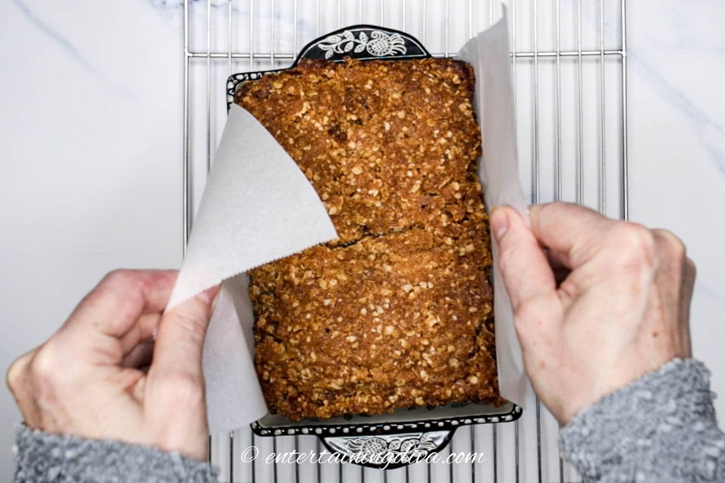 Banana nut bread being lifted out of the loaf pan with parchment paper