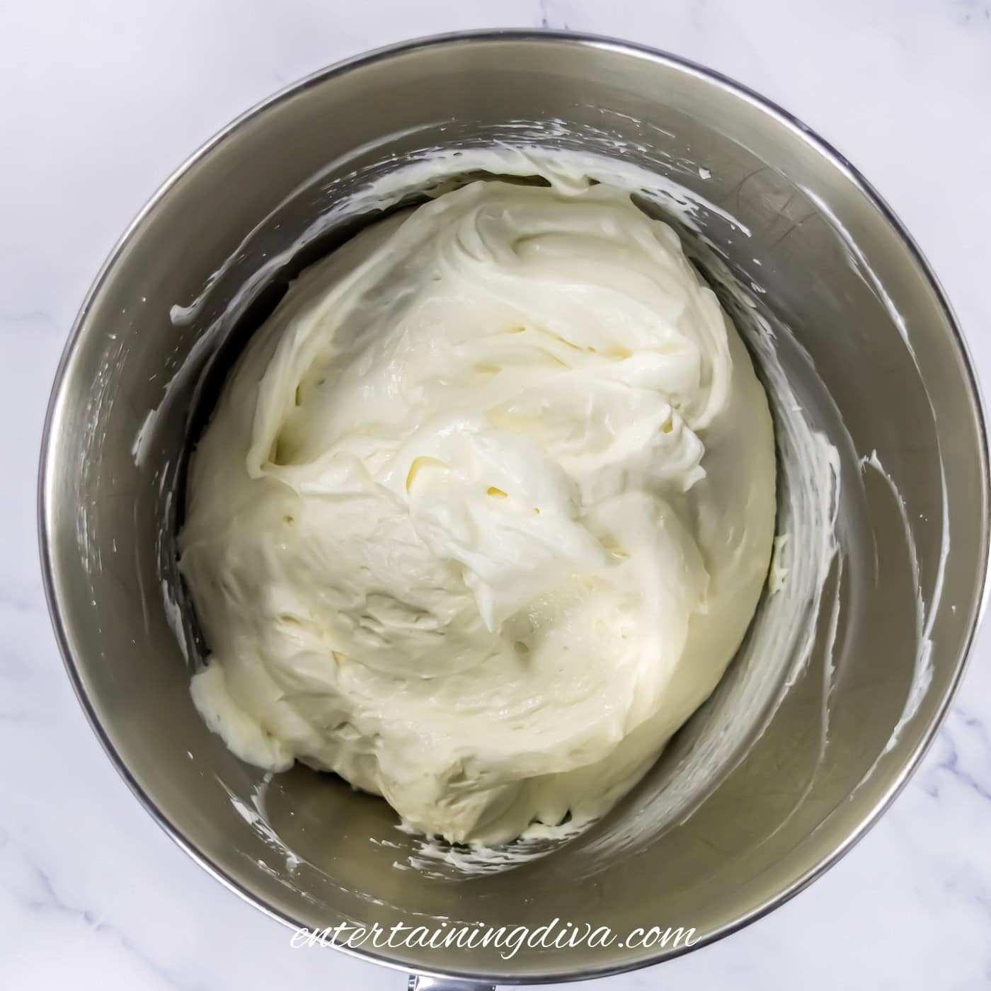 A metal mixing bowl filled with a cream cheese and whipped topping mixture, shown from above on a white surface.