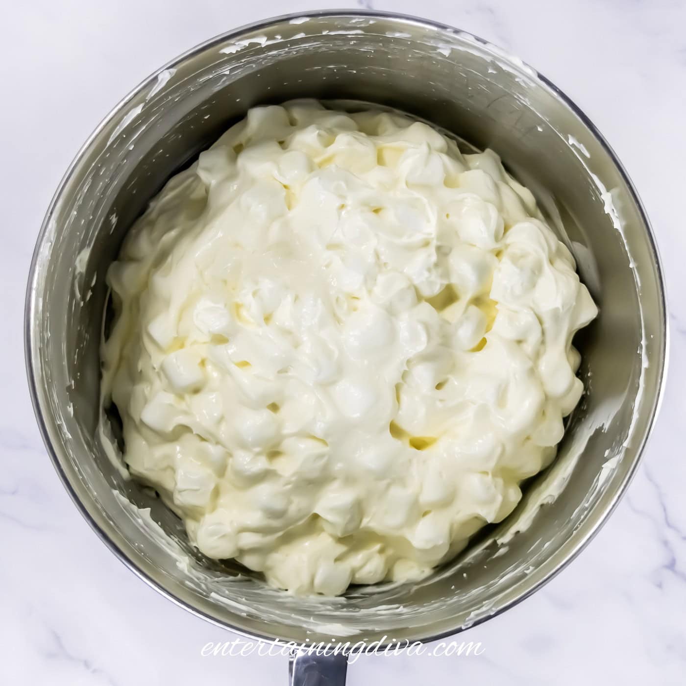 A stainless steel bowl filled with a cream cheese mixture and mini marshmallows.