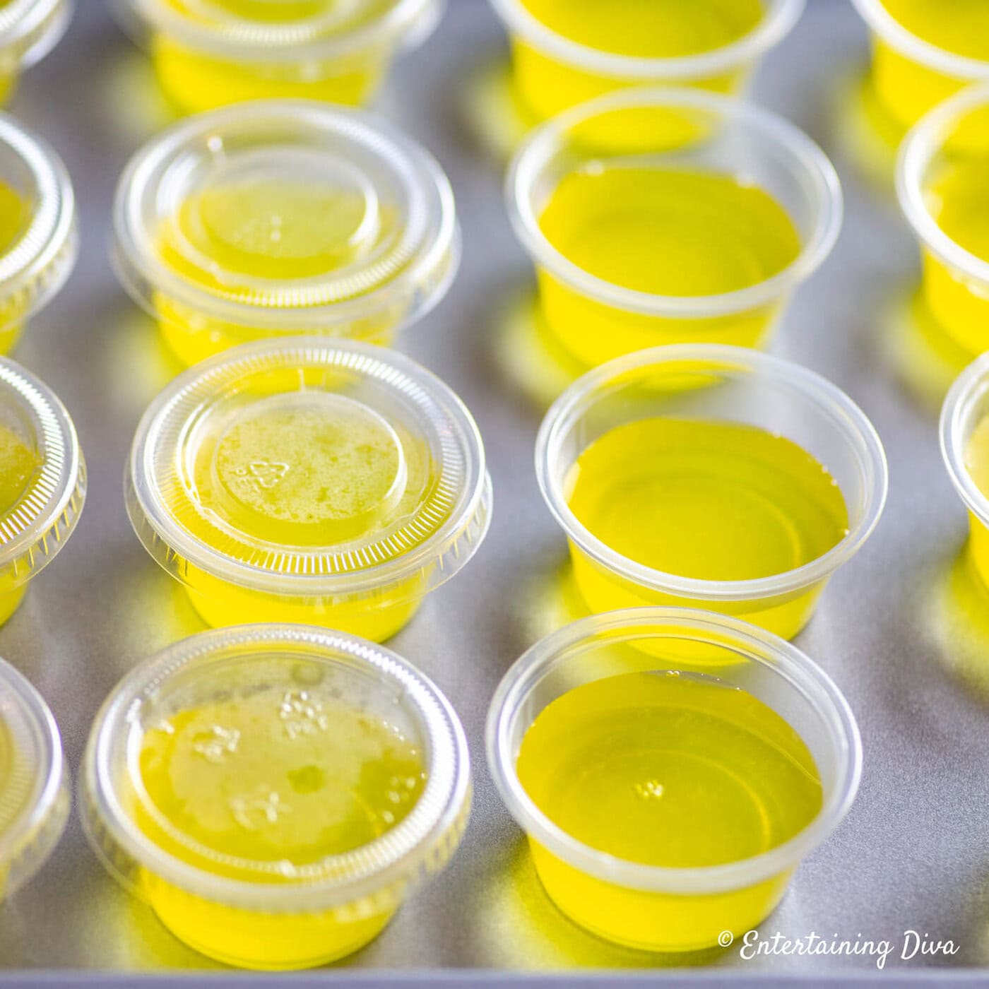 Yellow jello shots in jello shot cups, some with lids and some without