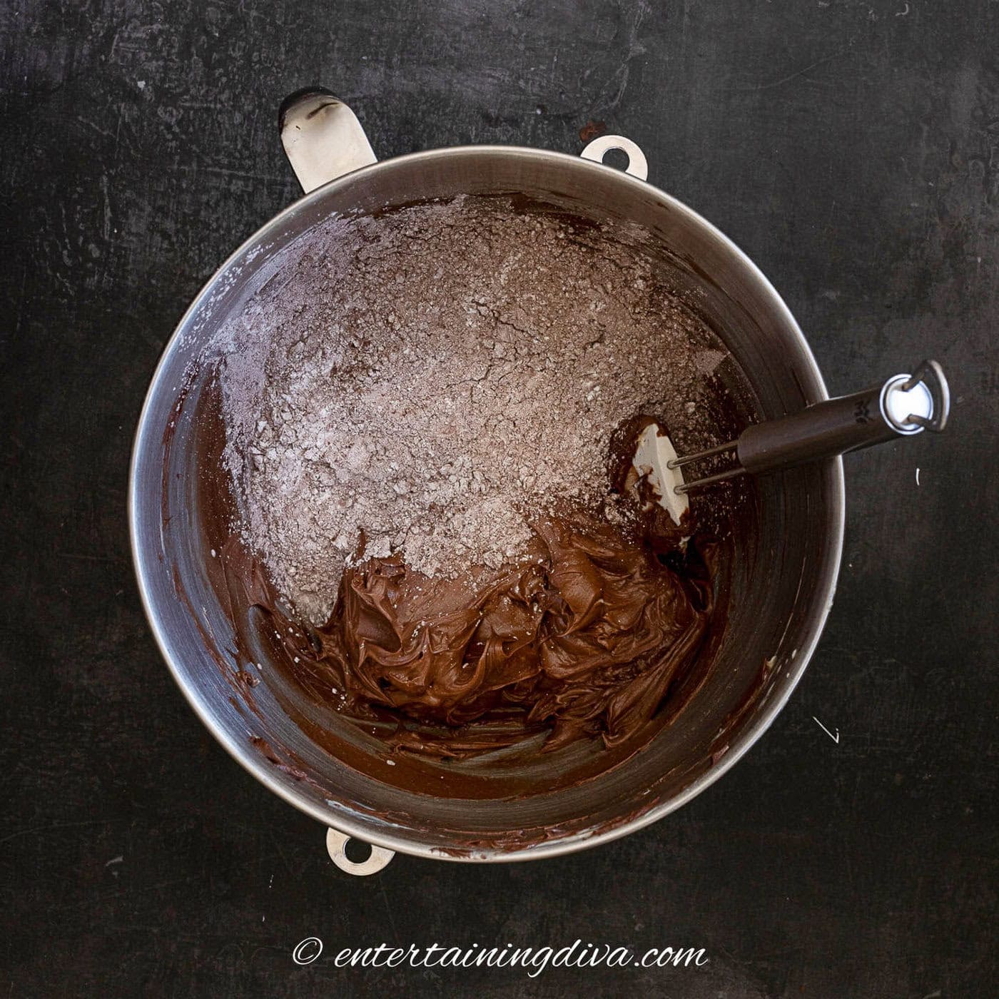 cocoa powder and icing sugar over chocolate frosting in a mixing bowl