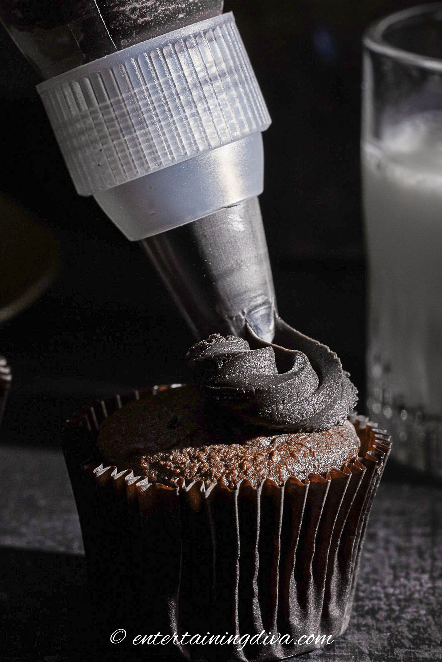 black chocolate frosting being piped onto a chocolate cupcake