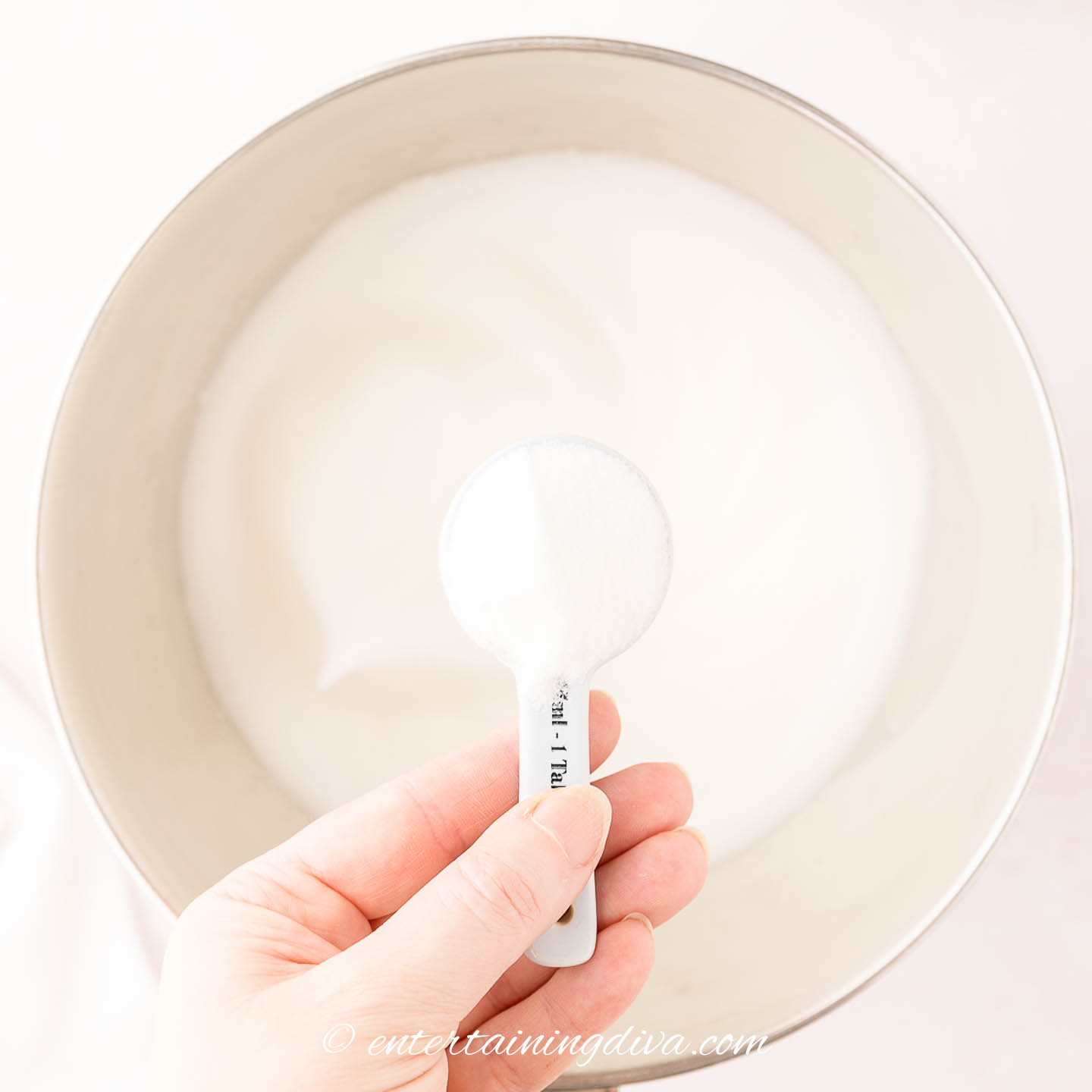 A tablespoon of sugar being added to the whipped egg whites