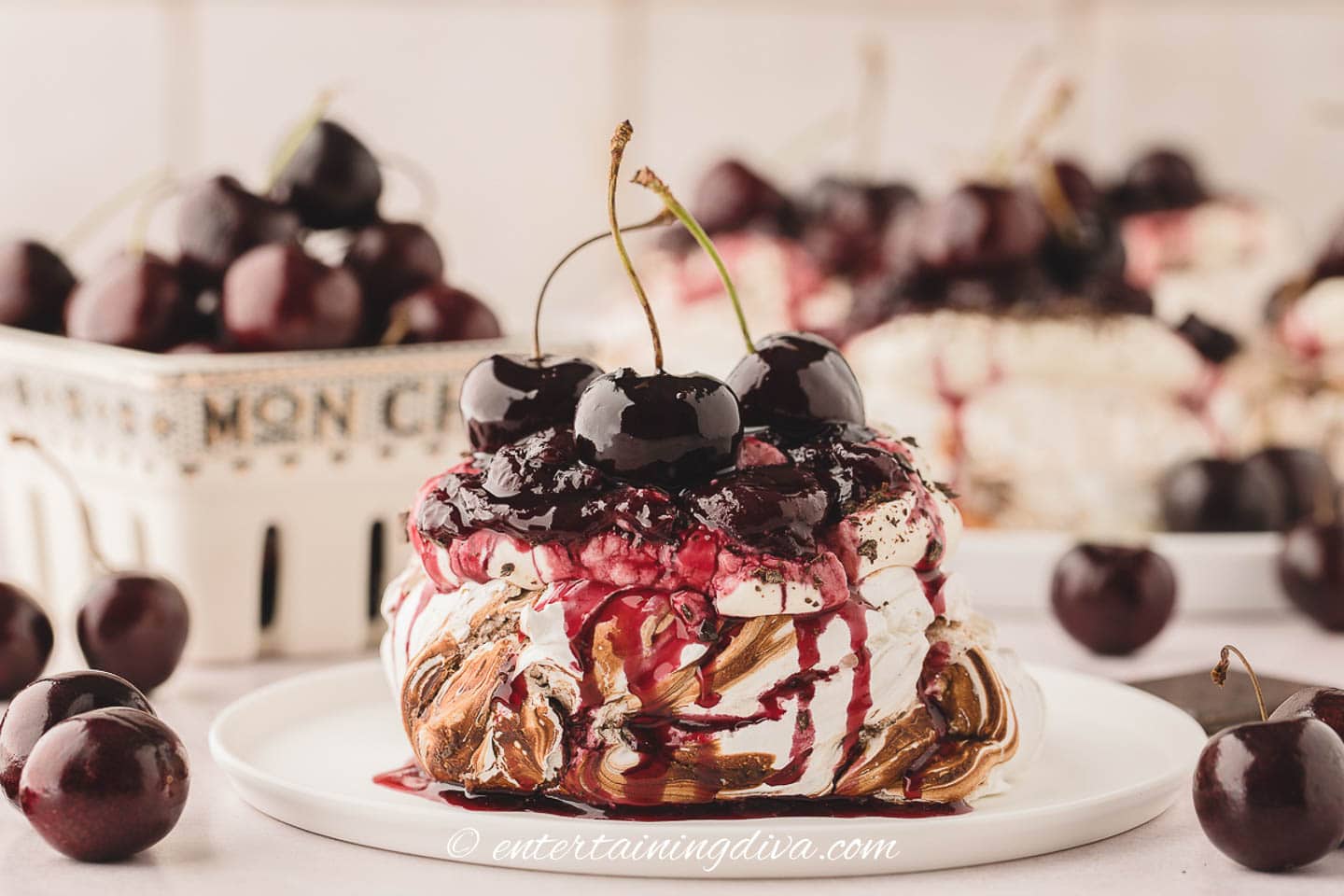 Black forest individual pavlova on a plate with cherries and more mini pavlovas in the background
