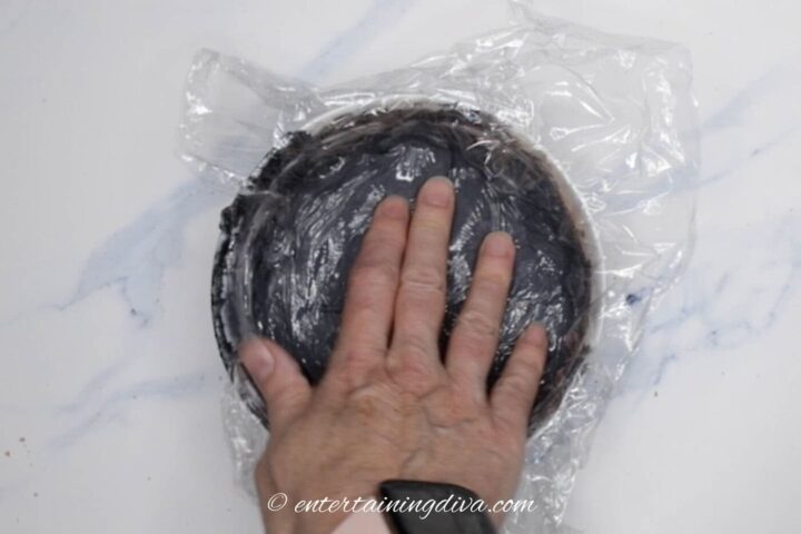 black royal icing in a bowl covered with plastic wrap