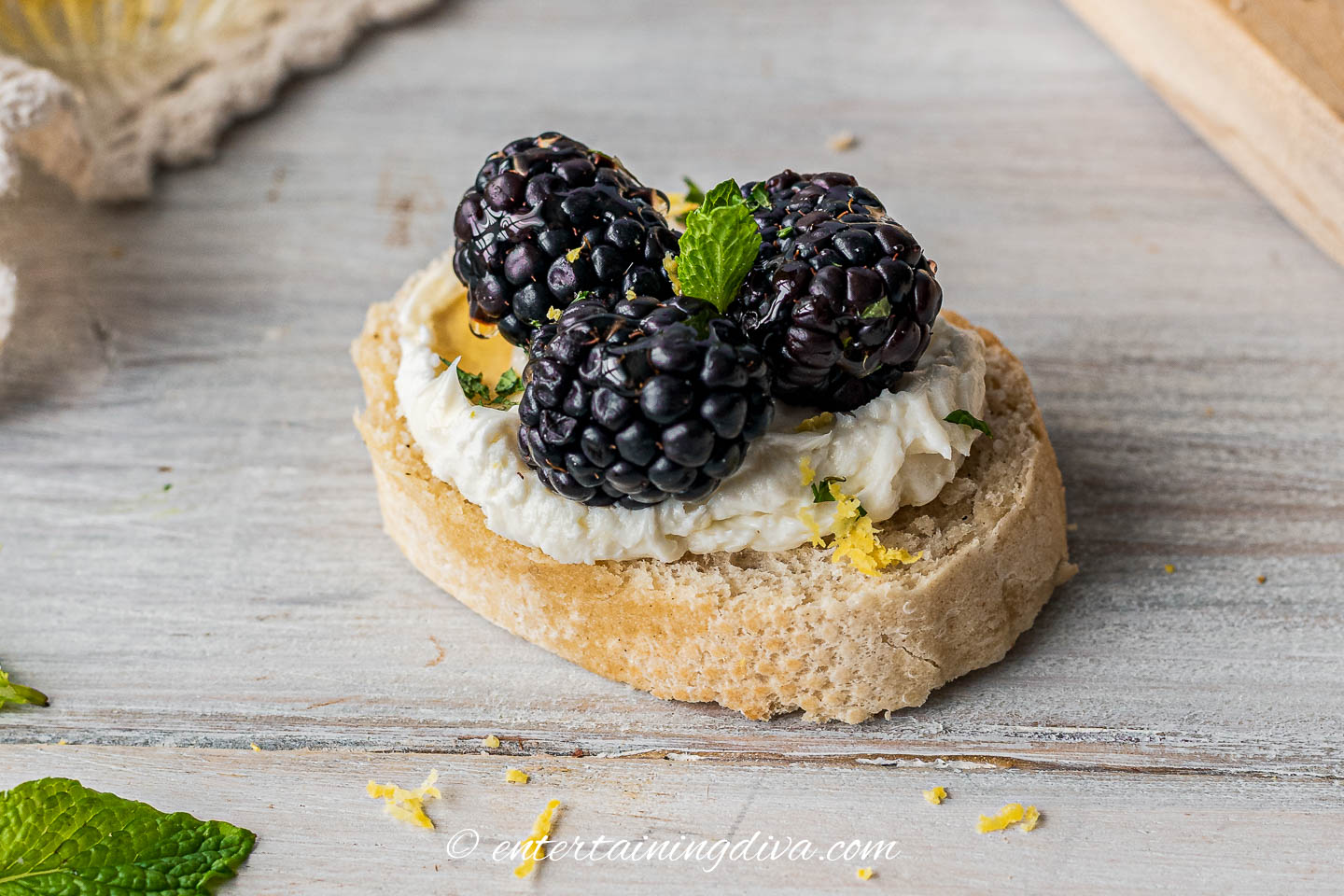 a blackberry goat cheese crostini garnished with mint and lemon zest
