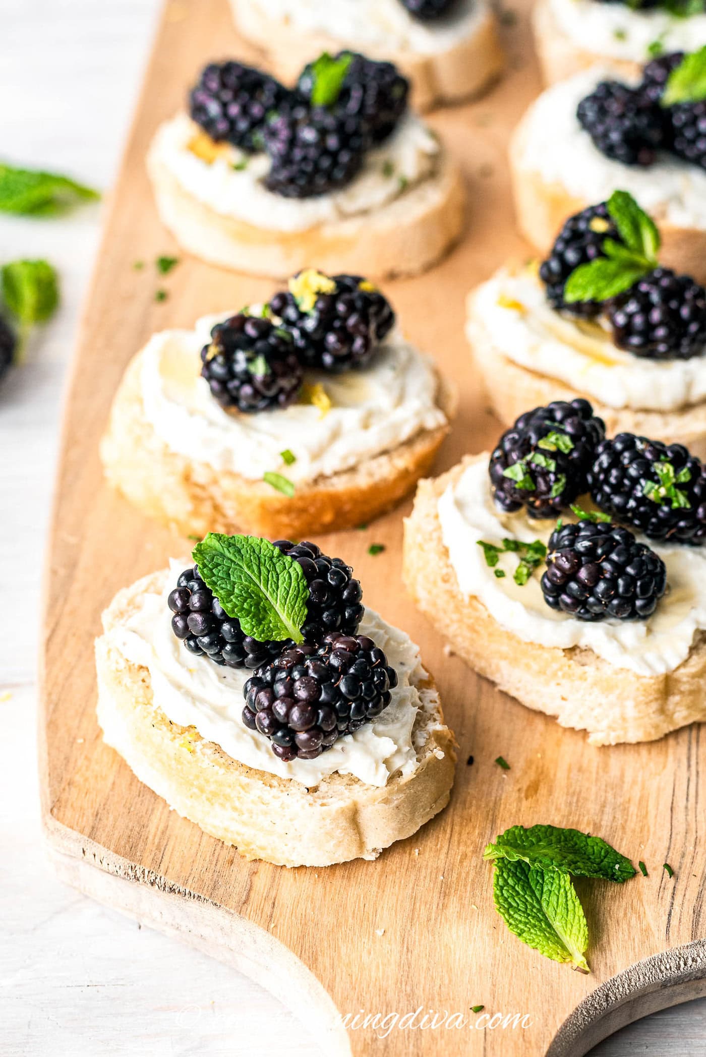 blackberry goat cheese crostini appetizers garnished with mint leaves on a cutting board