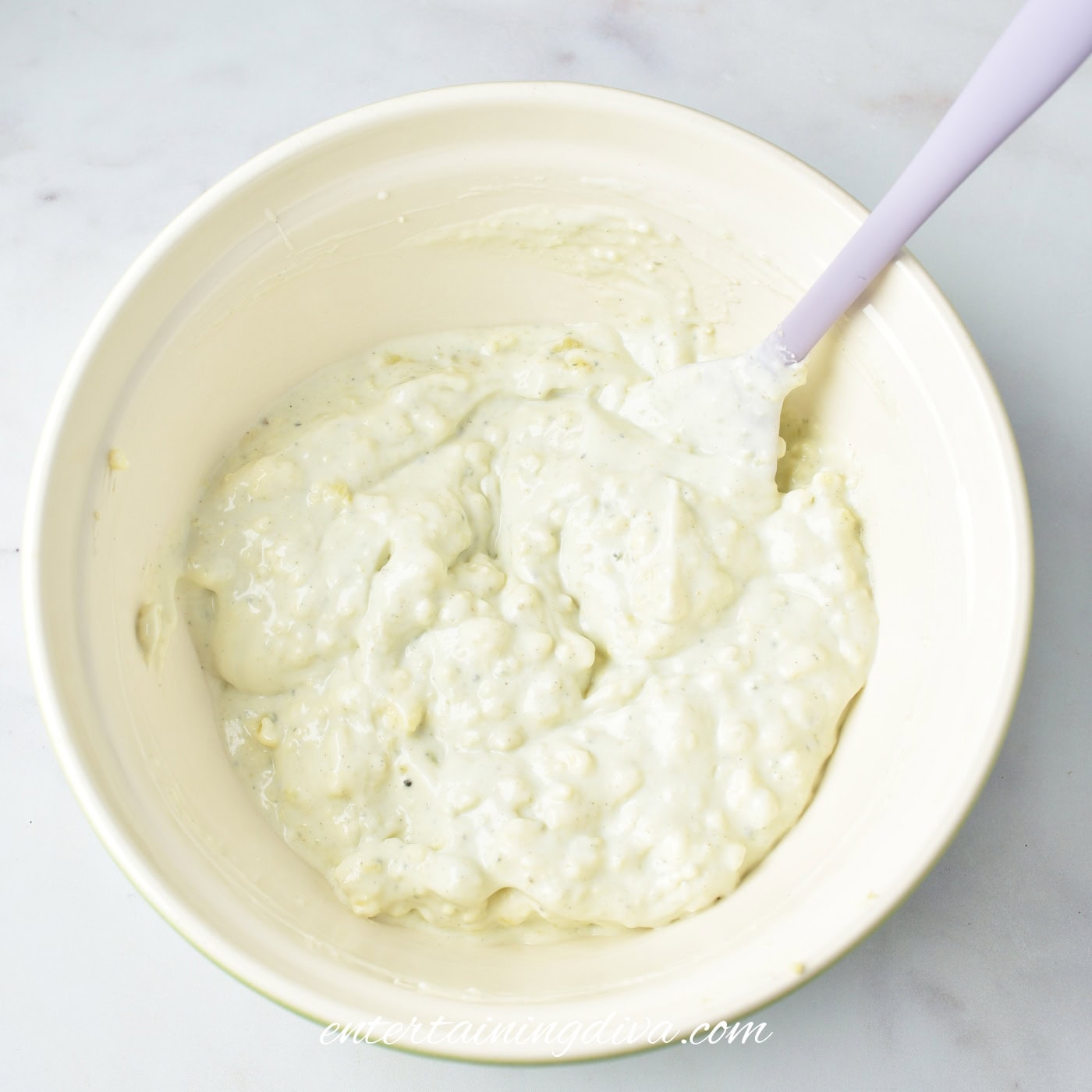 Mixed blue cheese dip in a white bowl and a spatula resting inside.