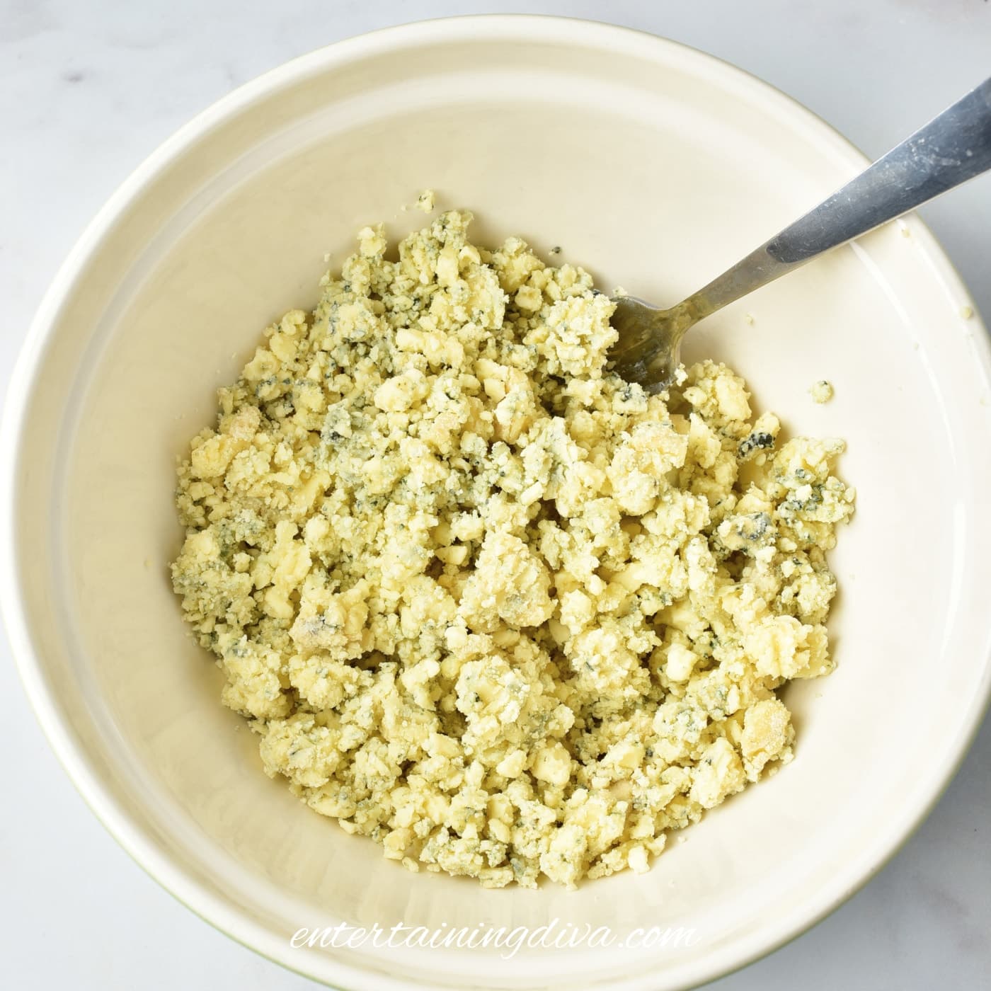 A bowl of crumbled blue cheese with a fork resting inside, on a white surface.