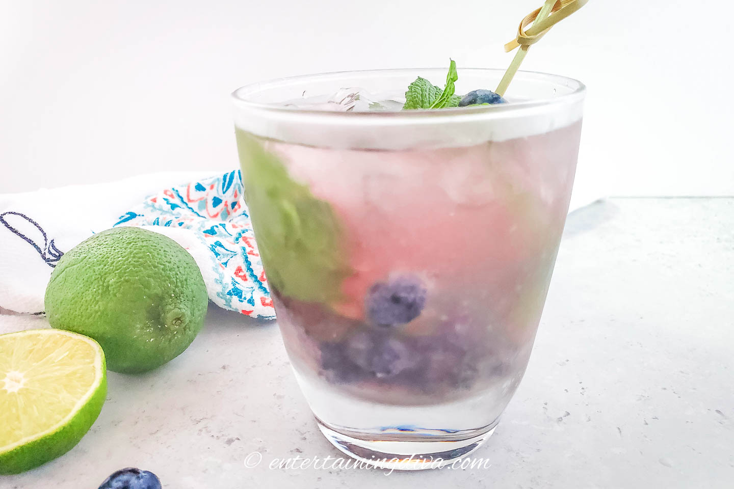 Side view of a fresh blueberry mojito and some limes
