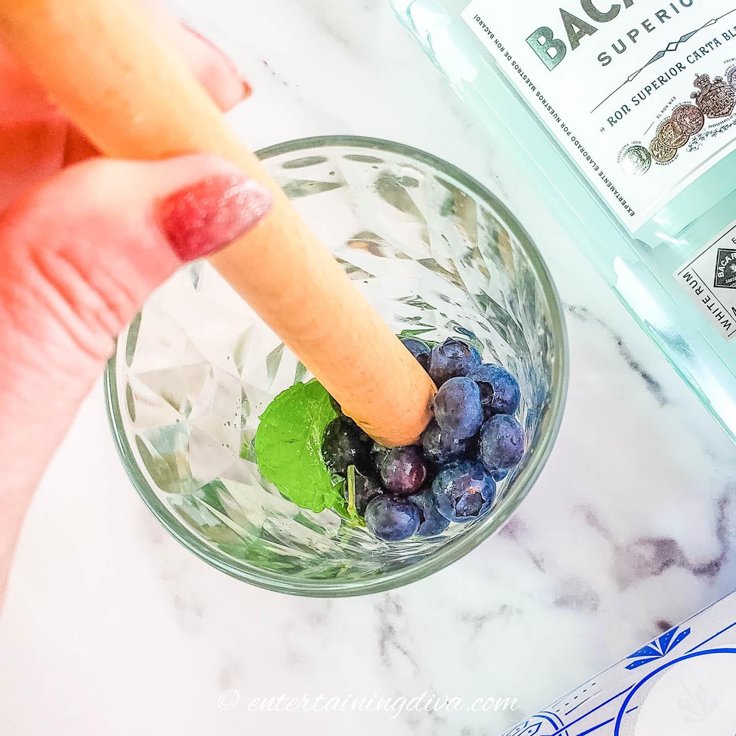 Blueberries, mint, sugar and lime juice being muddled in a glass