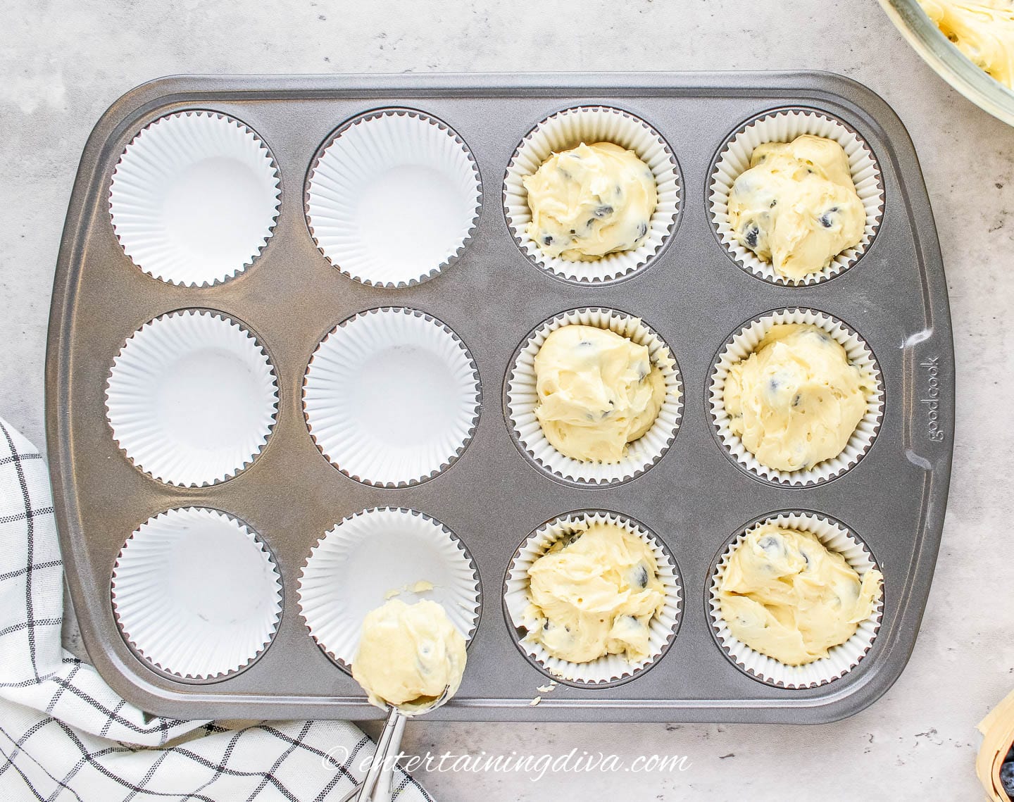 Muffin tins being filled with blueberry muffin batter