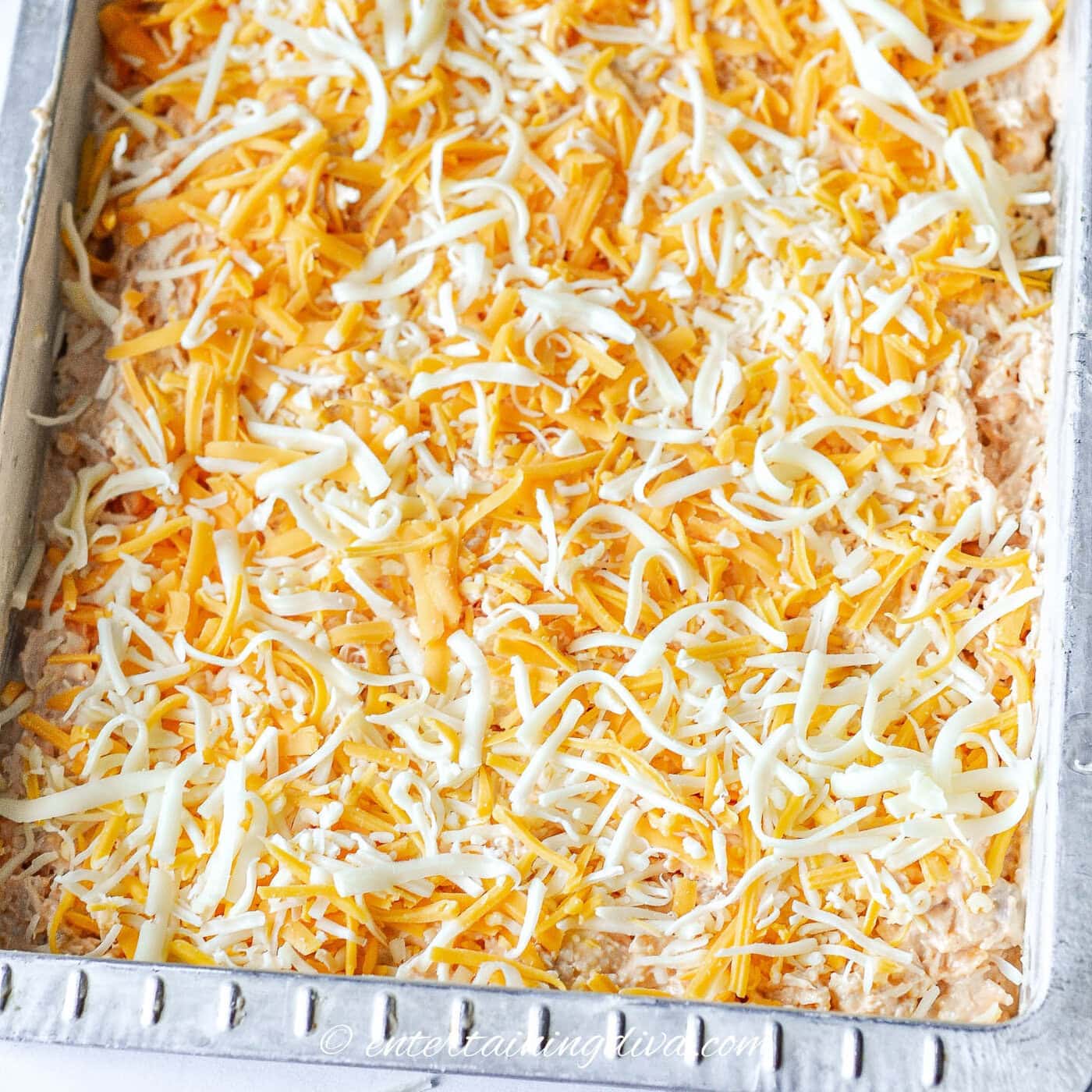 buffalo chicken dip with with grated cheese on top in a pan before being baked