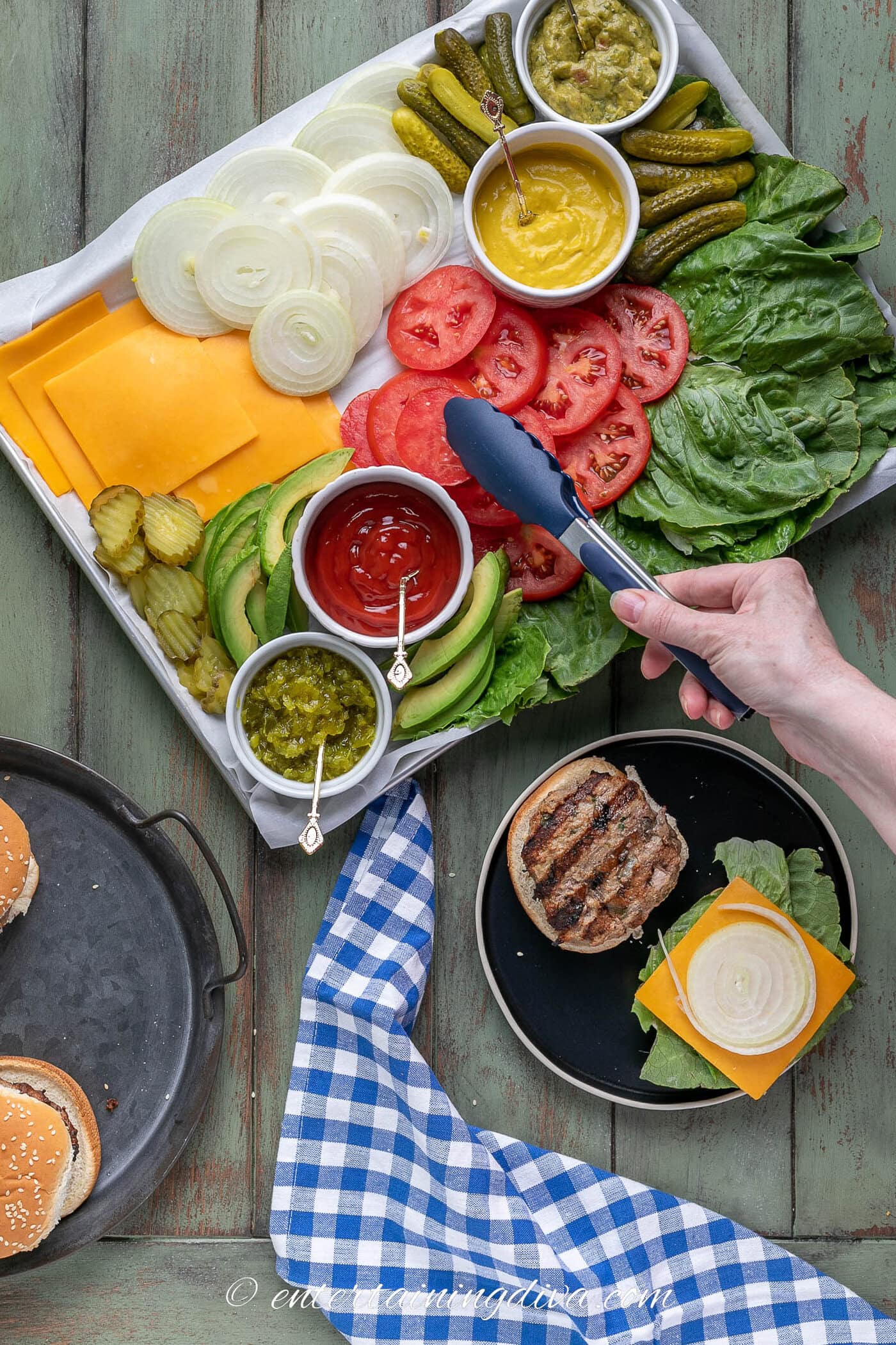 Tomato being taken from a burger toppings charcuterie board to put on a hamburger