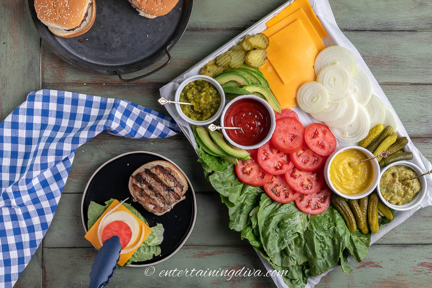 burger toppings charcuterie board beside a plate with a hamburger