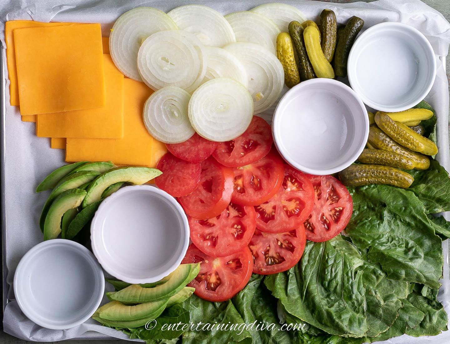 how to make a burger toppings charcuterie board step 6: bowls, lettuce, cheese, tomatoes, onions, dill pickles and avocado