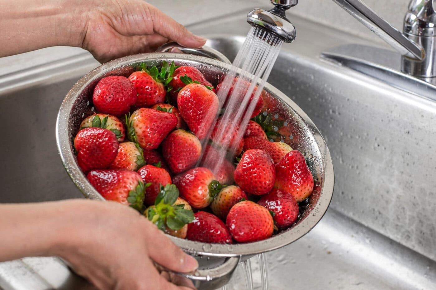 strawberries being washed in a colander