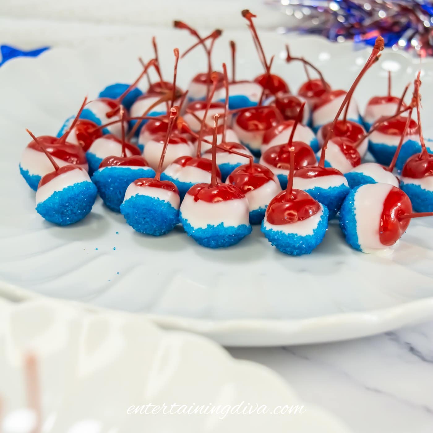 A plate of maraschino cherries dipped in white chocolate and blue sugar, arranged in rows for serving.