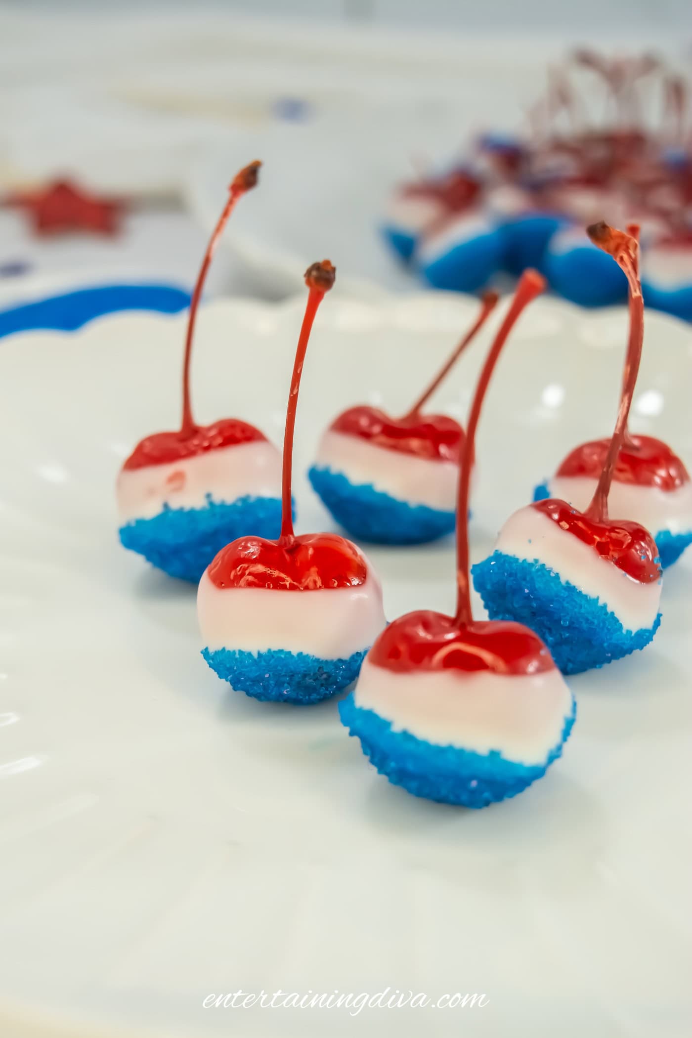 Five maraschino cherries dipped in white chocolate and blue sugar, arranged on a white plate.
