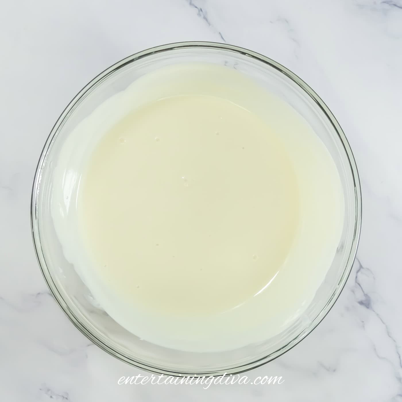 A clear glass bowl filled with a creamy white liquid is placed on a white marble surface.
