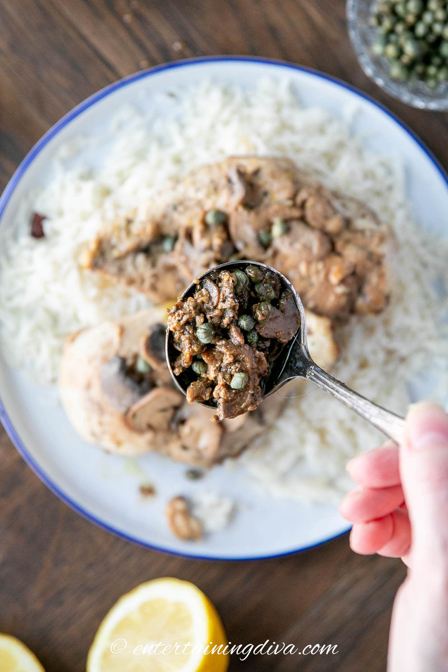 Piccata sauce with mushrooms in a spoon over a plate with chicken breasts and rice
