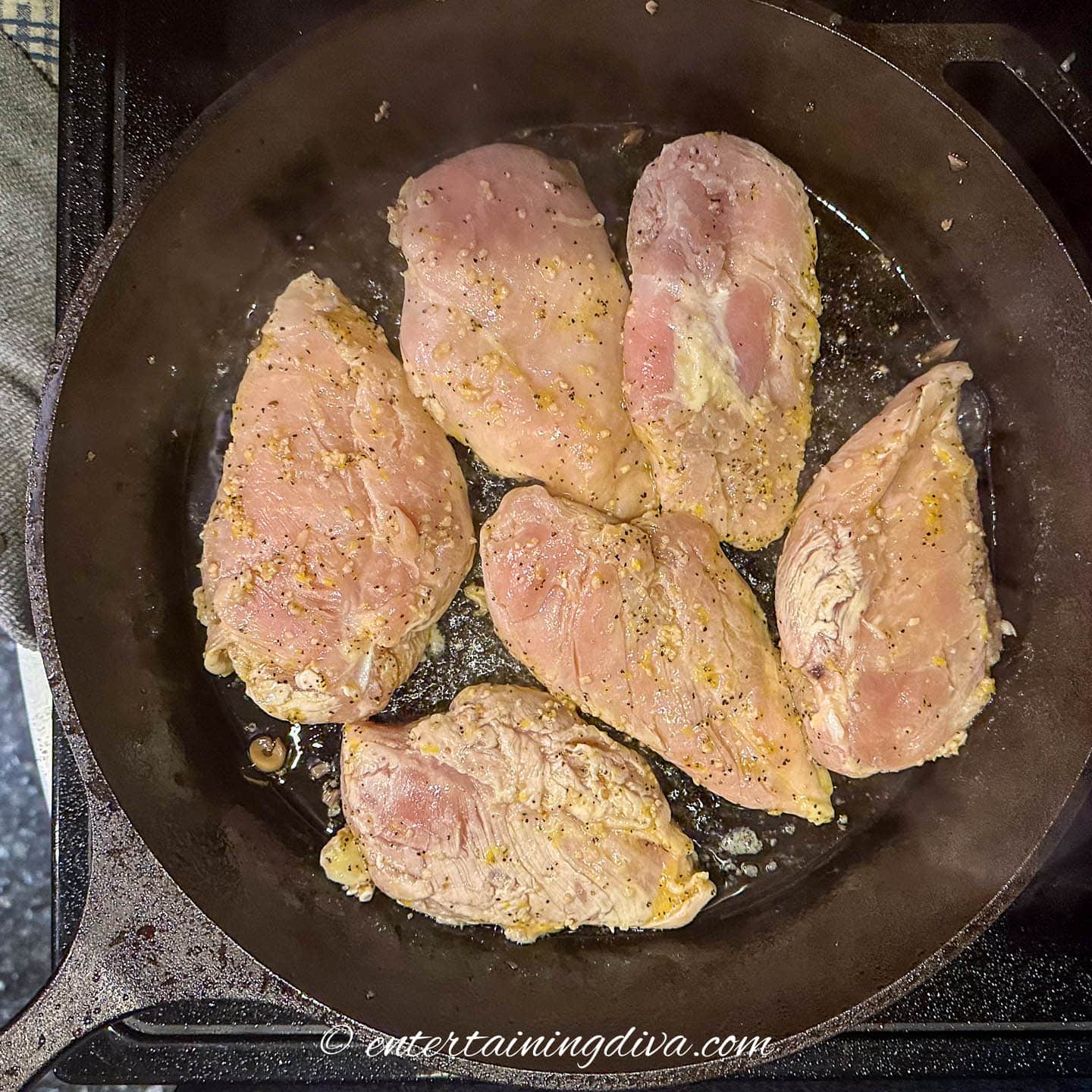 chicken breasts cooking in a cast iron pan