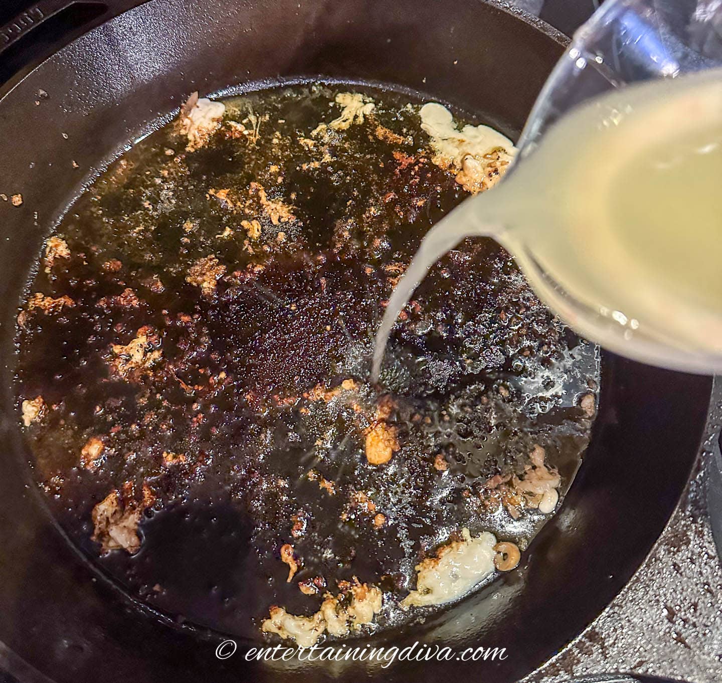 chicken stock being poured into a cast iron pan