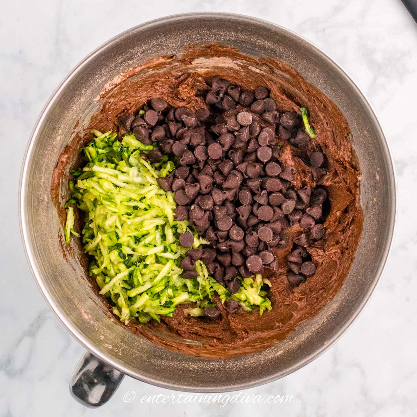 grated zucchini and chocolate chips on top of chocolate zucchini bread batter in a mixing bowl