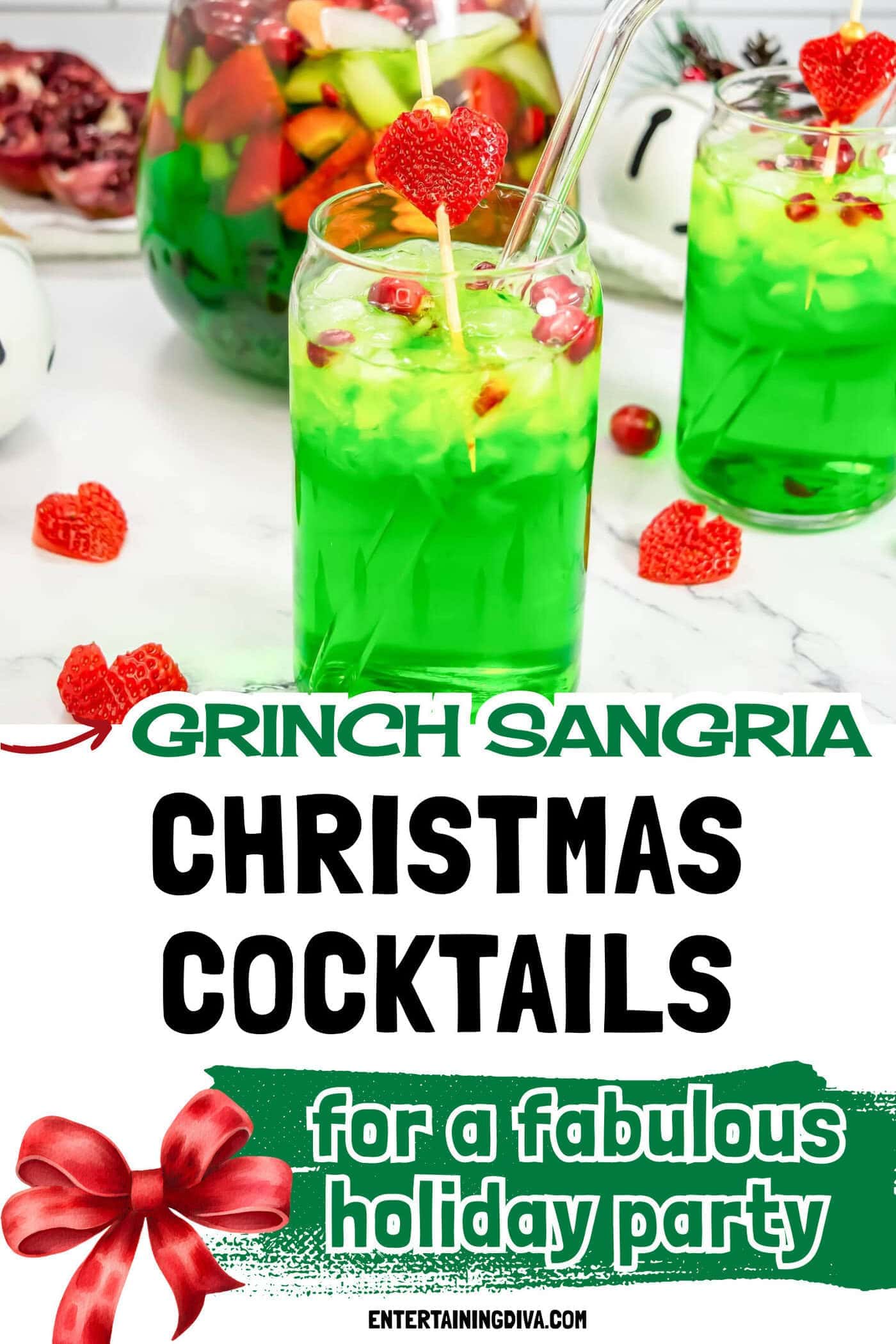 A glass of bright green drink with ice, pomegranate seeds, and a skewer topped with a heart-shaped strawberry; a pitcher of fruit punch and more fruit are in the background.