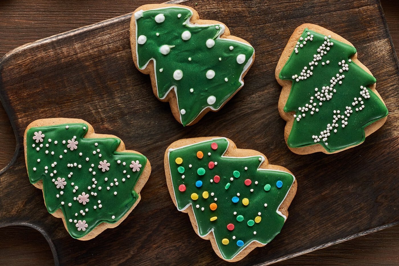 Four different Christmas tree cookie designs displayed on a rustic wooden cutting board.