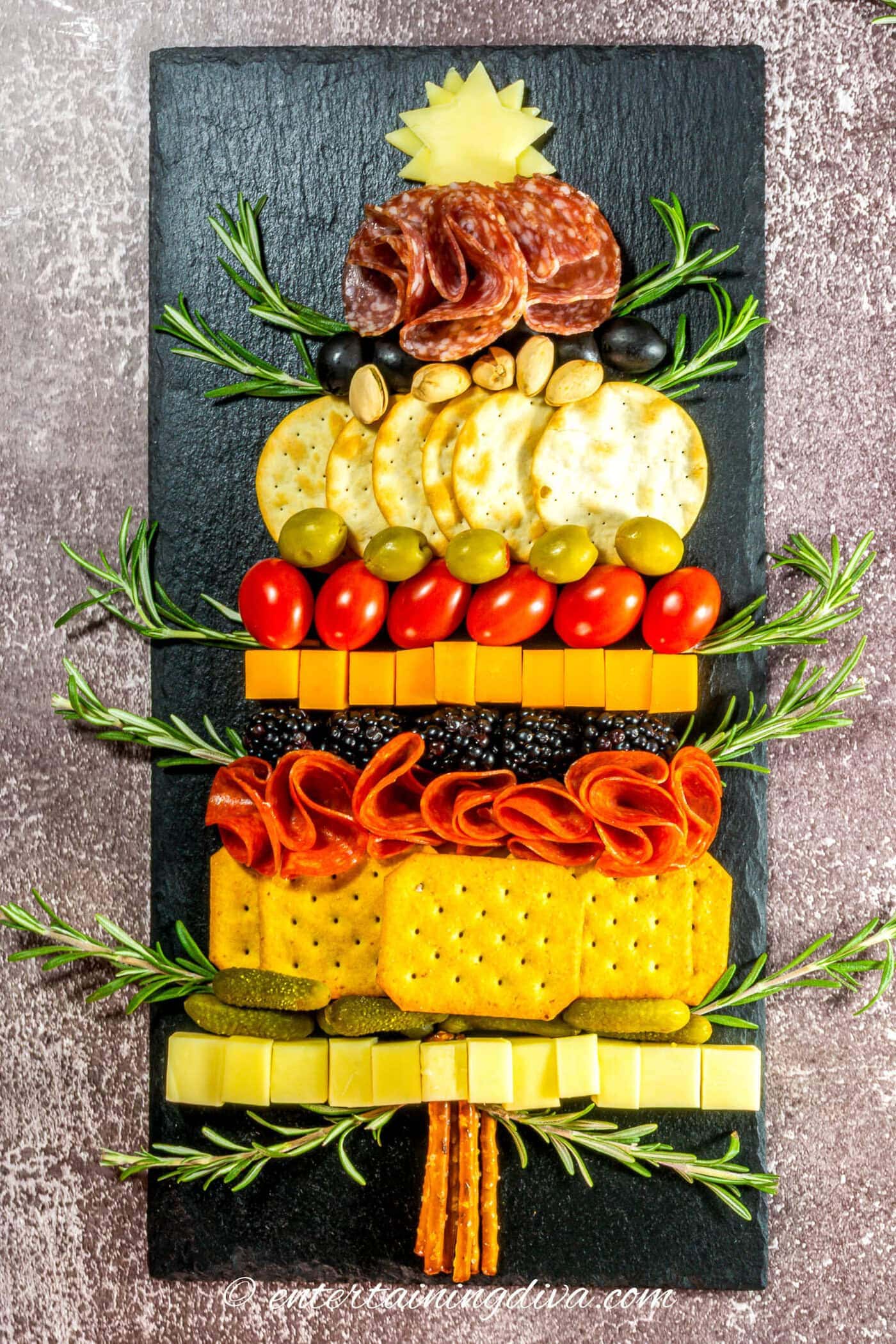 A Christmas tree charcuterie board garnished with rosemary "branches"