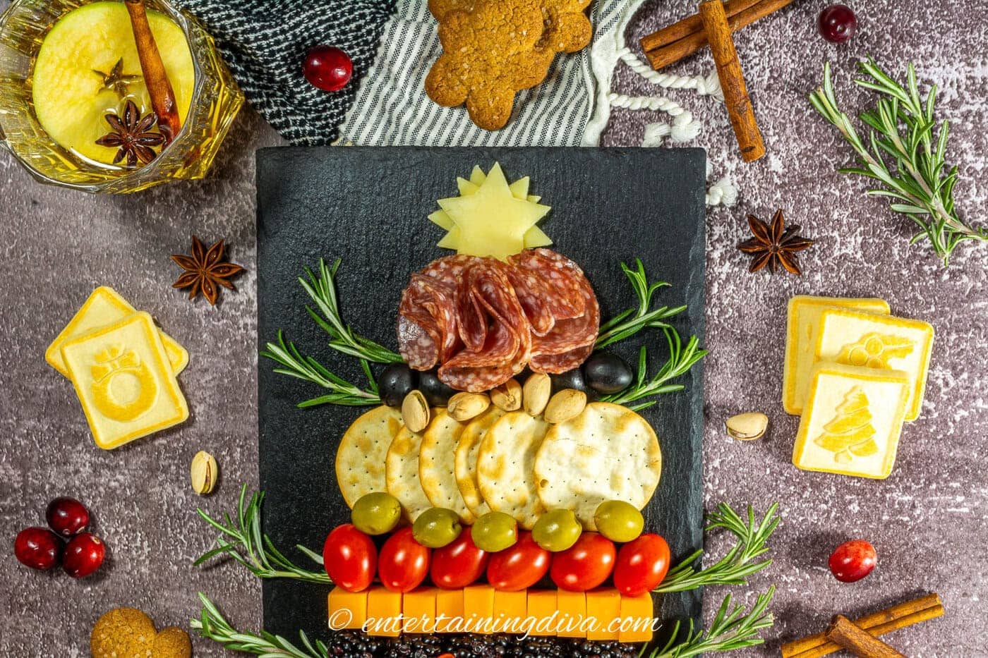 The top of a Christmas tree charcuterie board surrounded by Christmas crackers, cranberries, rosemary and cinnamon sticks