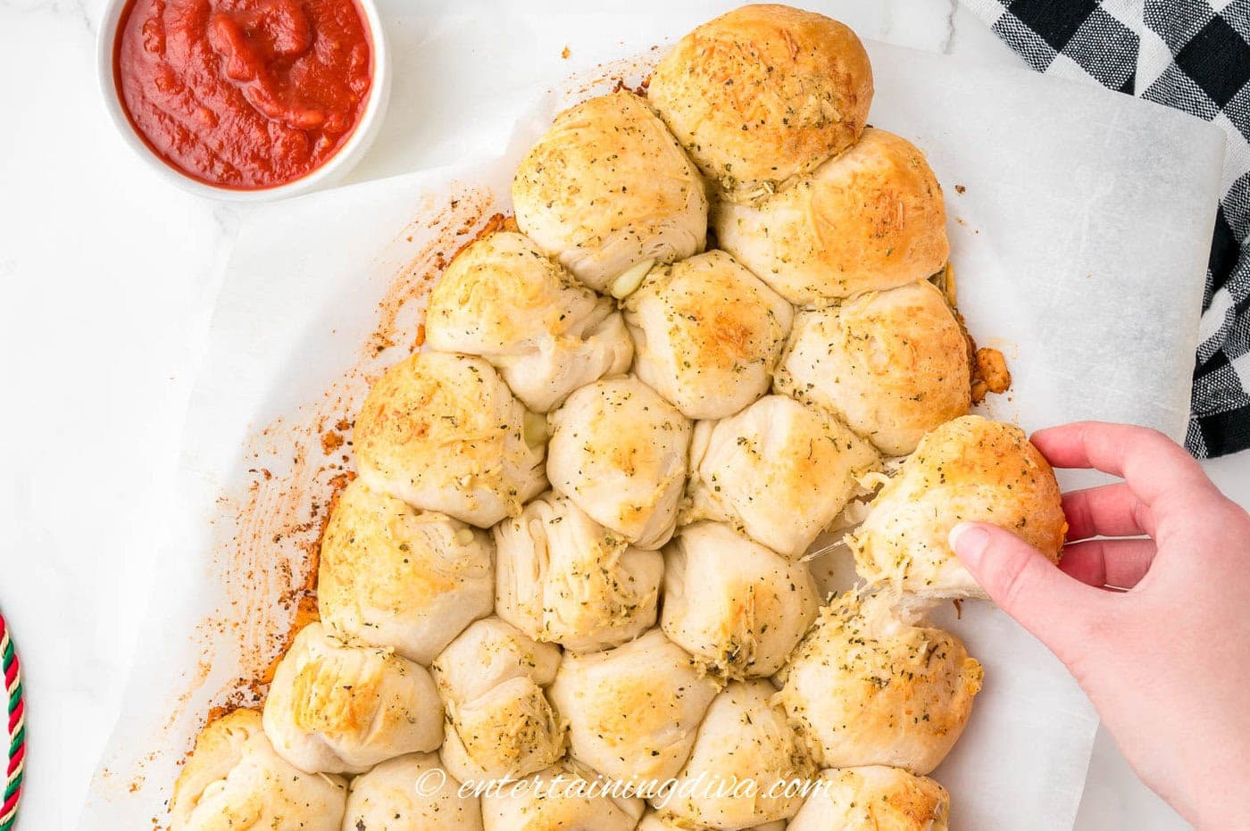A Christmas tree pull apart bread beside a bowl of marinara sauce