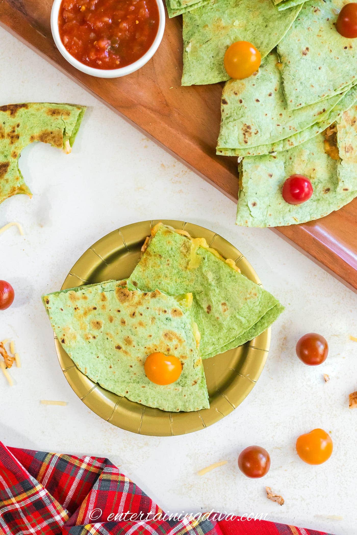 Two pieces of quesadilla on a plate beside a Christmas tree quesadilla