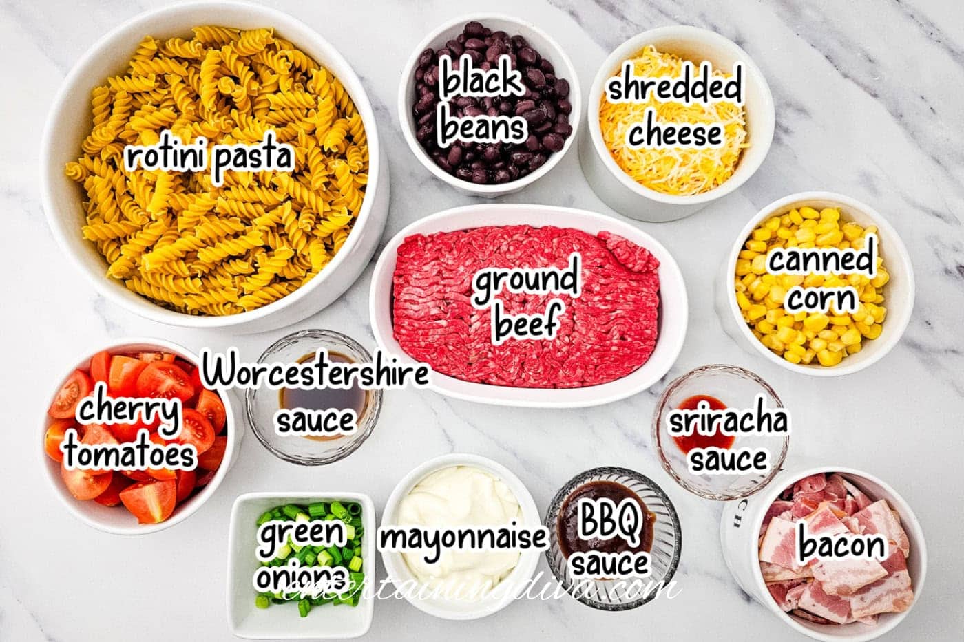 Cowboy pasta ingredients including rotini pasta, black beans, shredded cheese, ground beef, canned corn, cherry tomatoes, Worcestershire sauce, green onions, mayonnaise, BBQ sauce, sriracha sauce, and bacon.