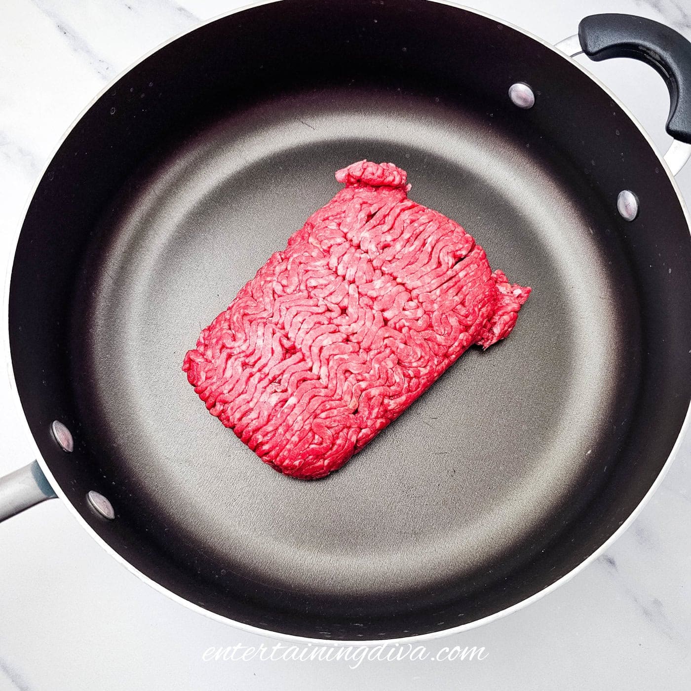 Raw ground beef in a nonstick frying pan.