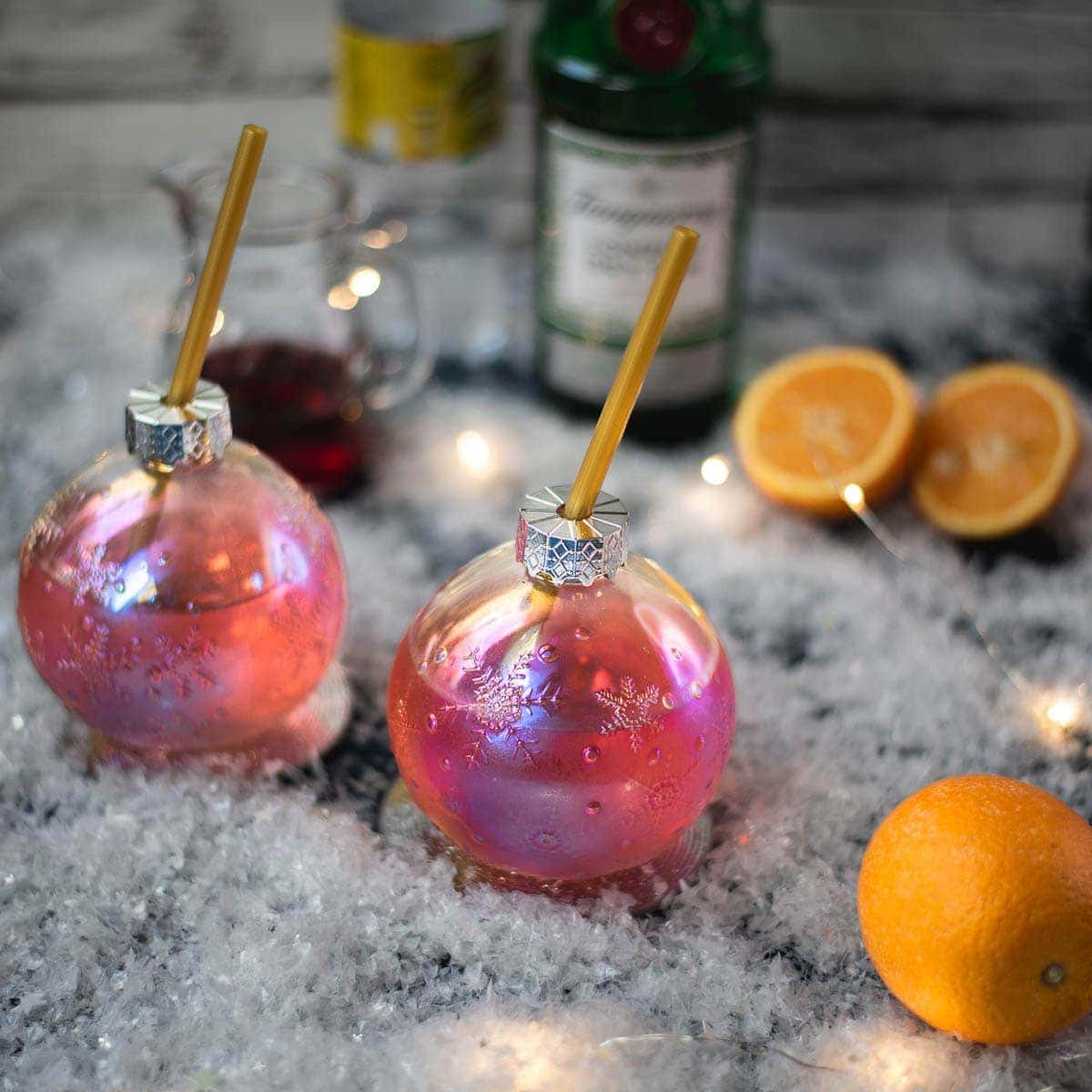 Two pink baubles on a table next to oranges and a bottle of wine.