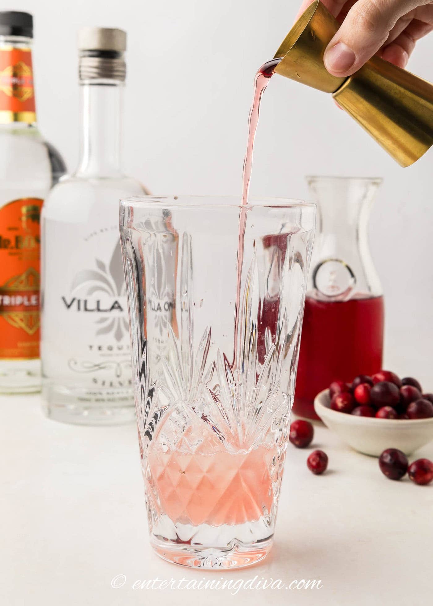 cranberry juice being poured into a shaker with tequila