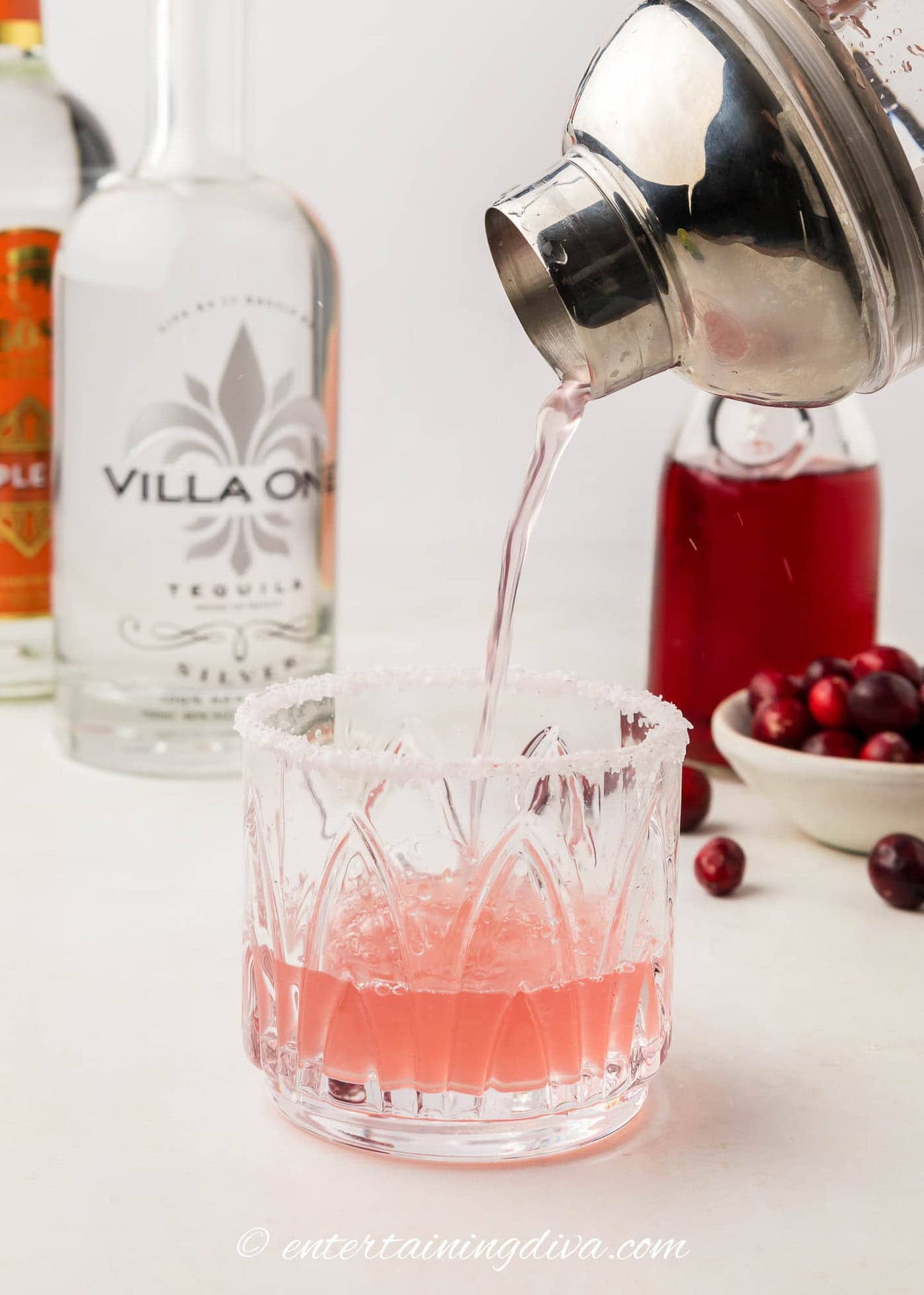 cranberry margarita being poured from a shaker into a glass