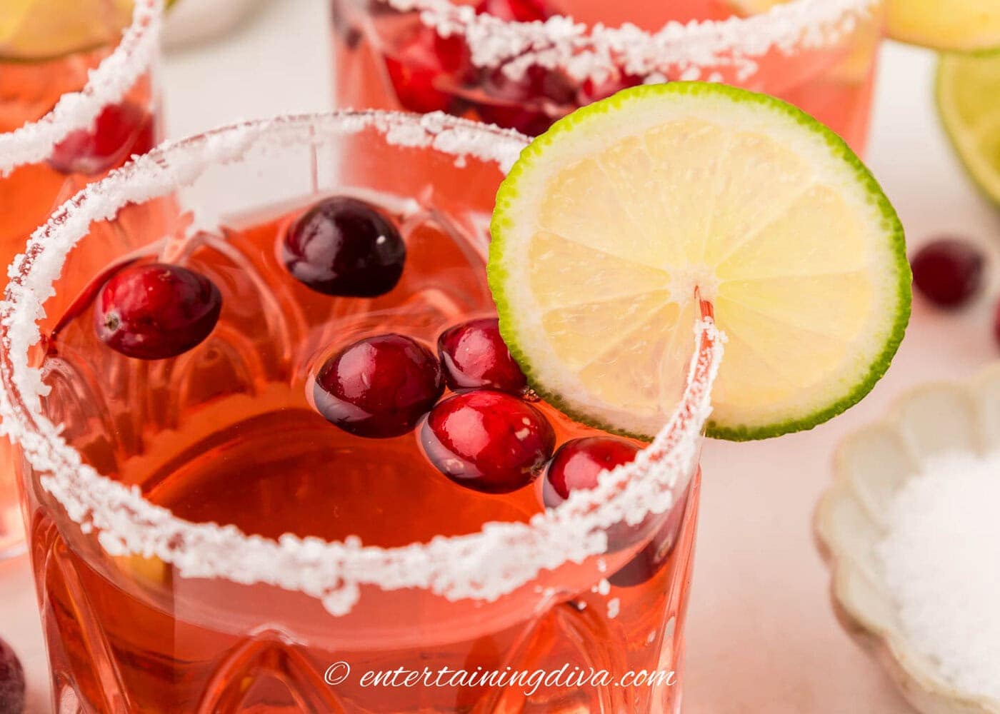 Close up of a lime wheel and fresh cranberries garnishing a Christmas margarita cocktail