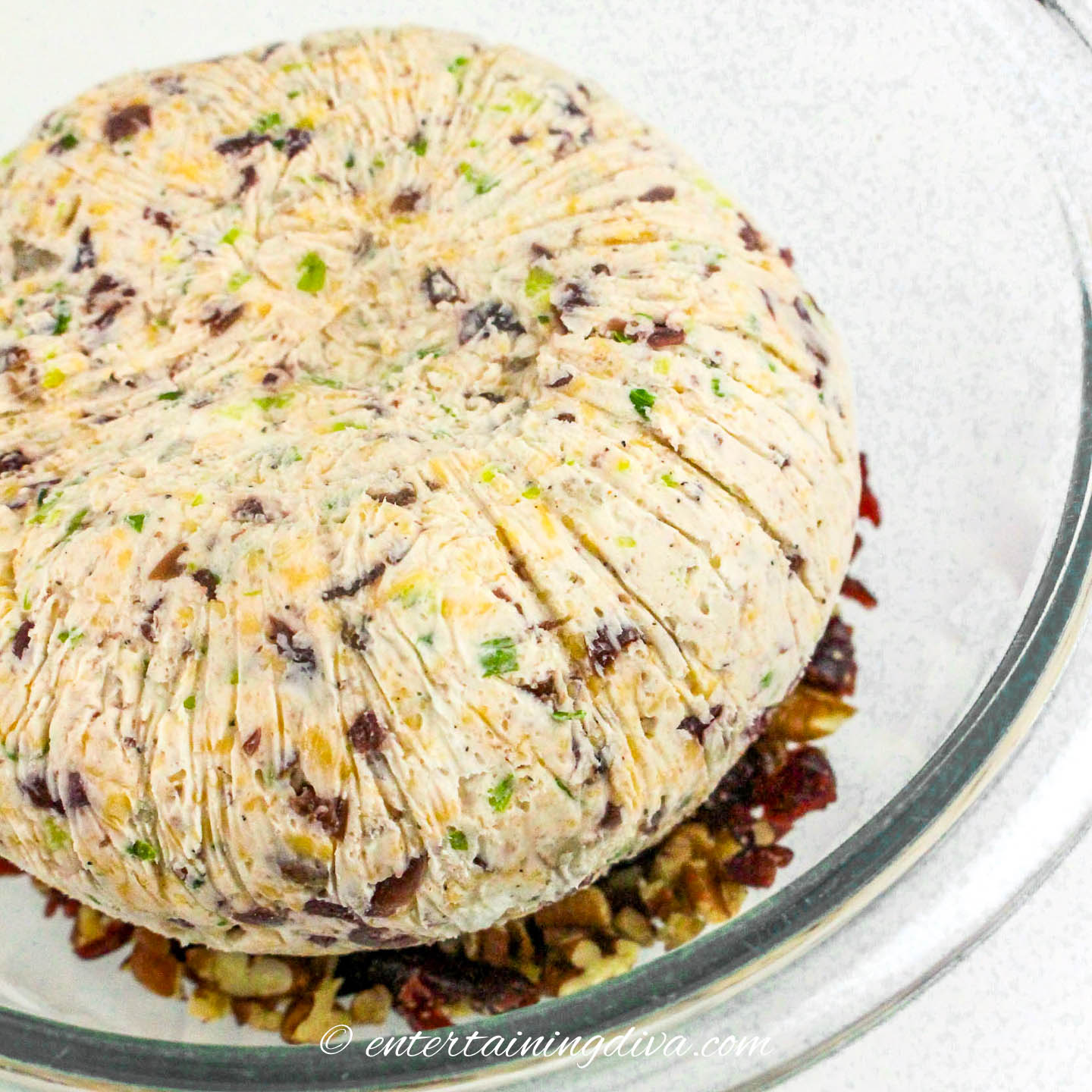 cranberry pecan cheese ball in a bowl with chopped pecans and cranberries