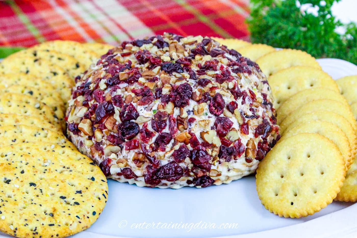 A cranberry pecan cheese ball on a plane surrounded by crackers