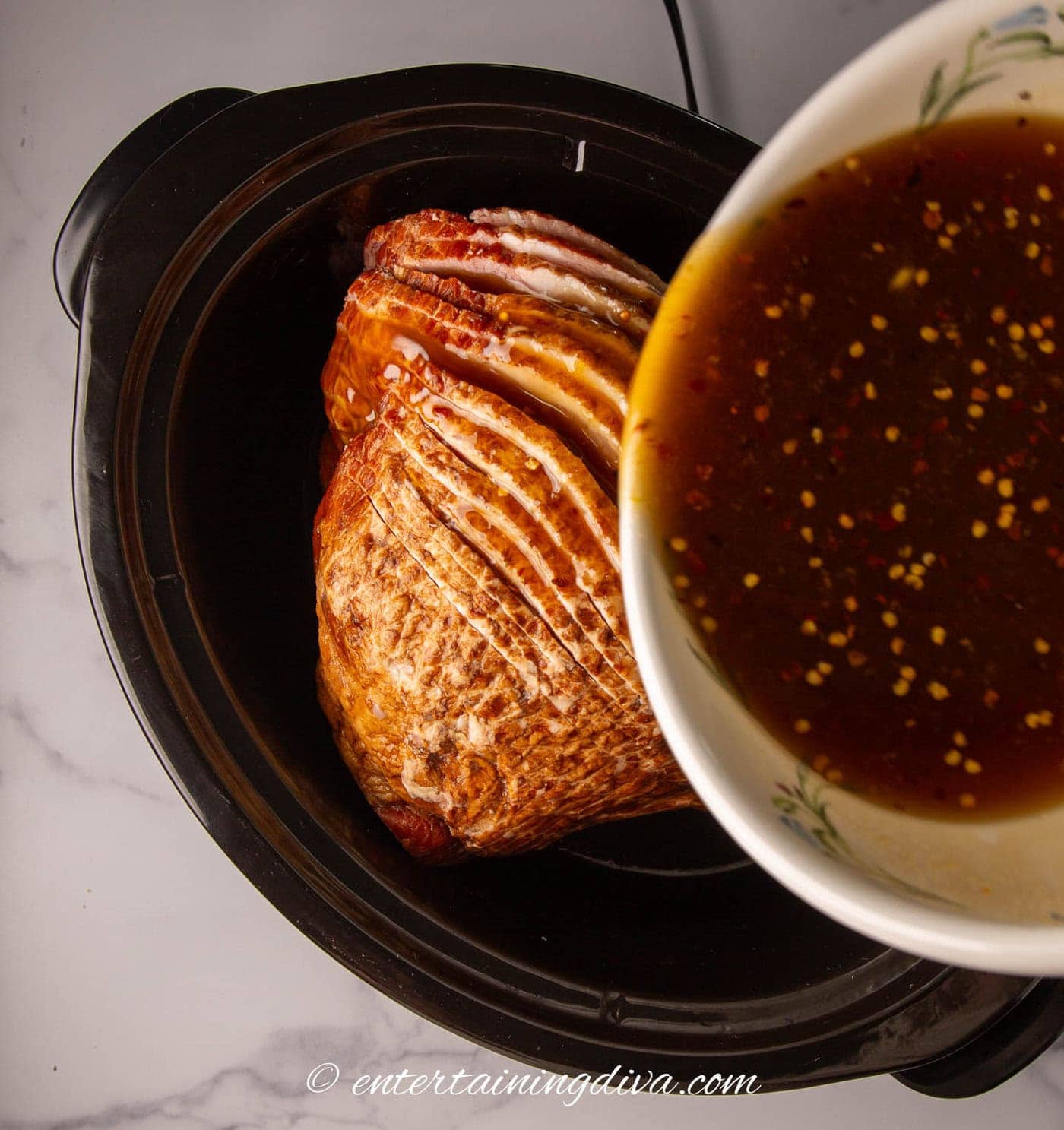 pineapple juice and brown sugar marinade being poured over a ham in a crock pot