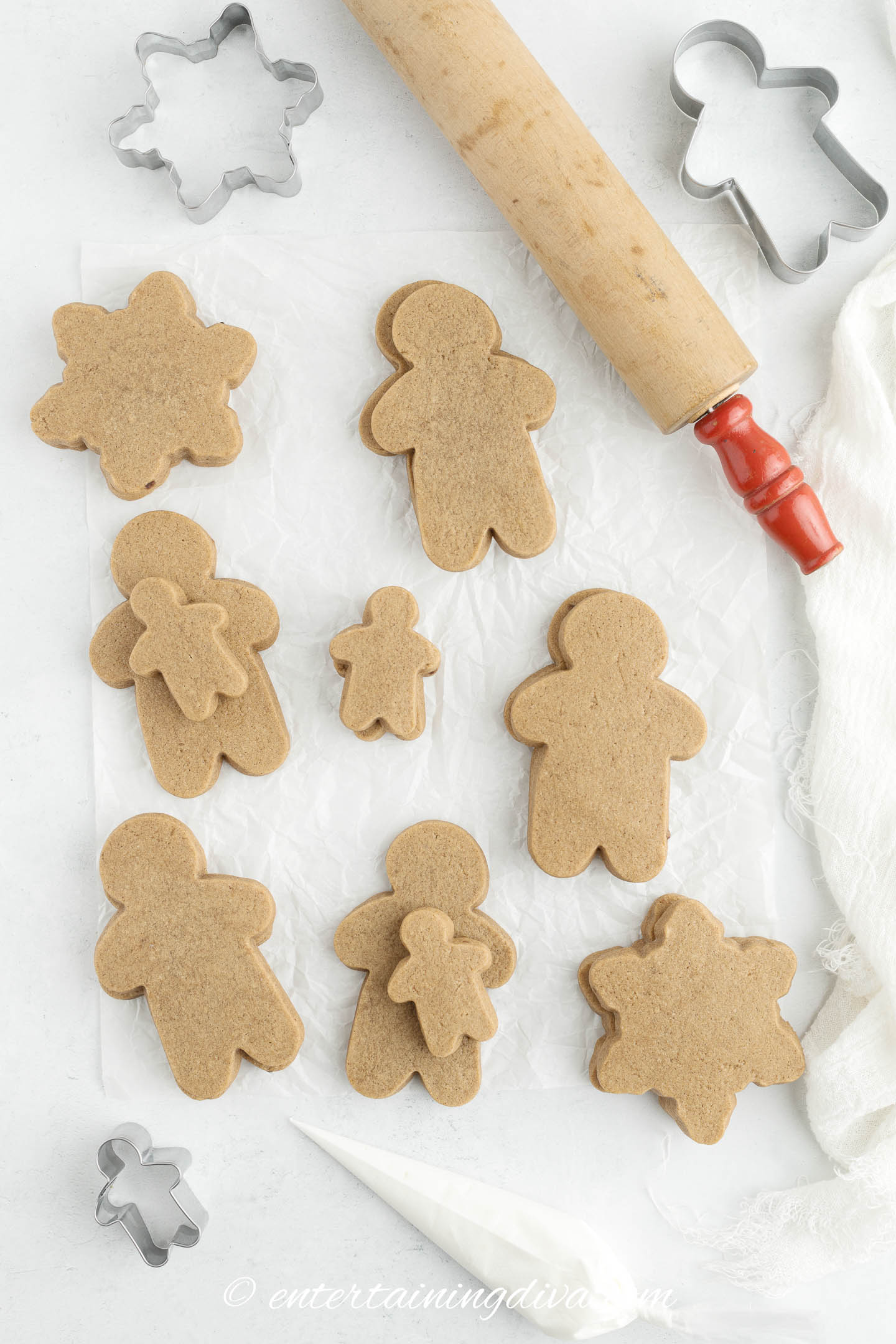cut out gingerbread men and snowflakes on a countertop with cookie cutters and a rolling pin