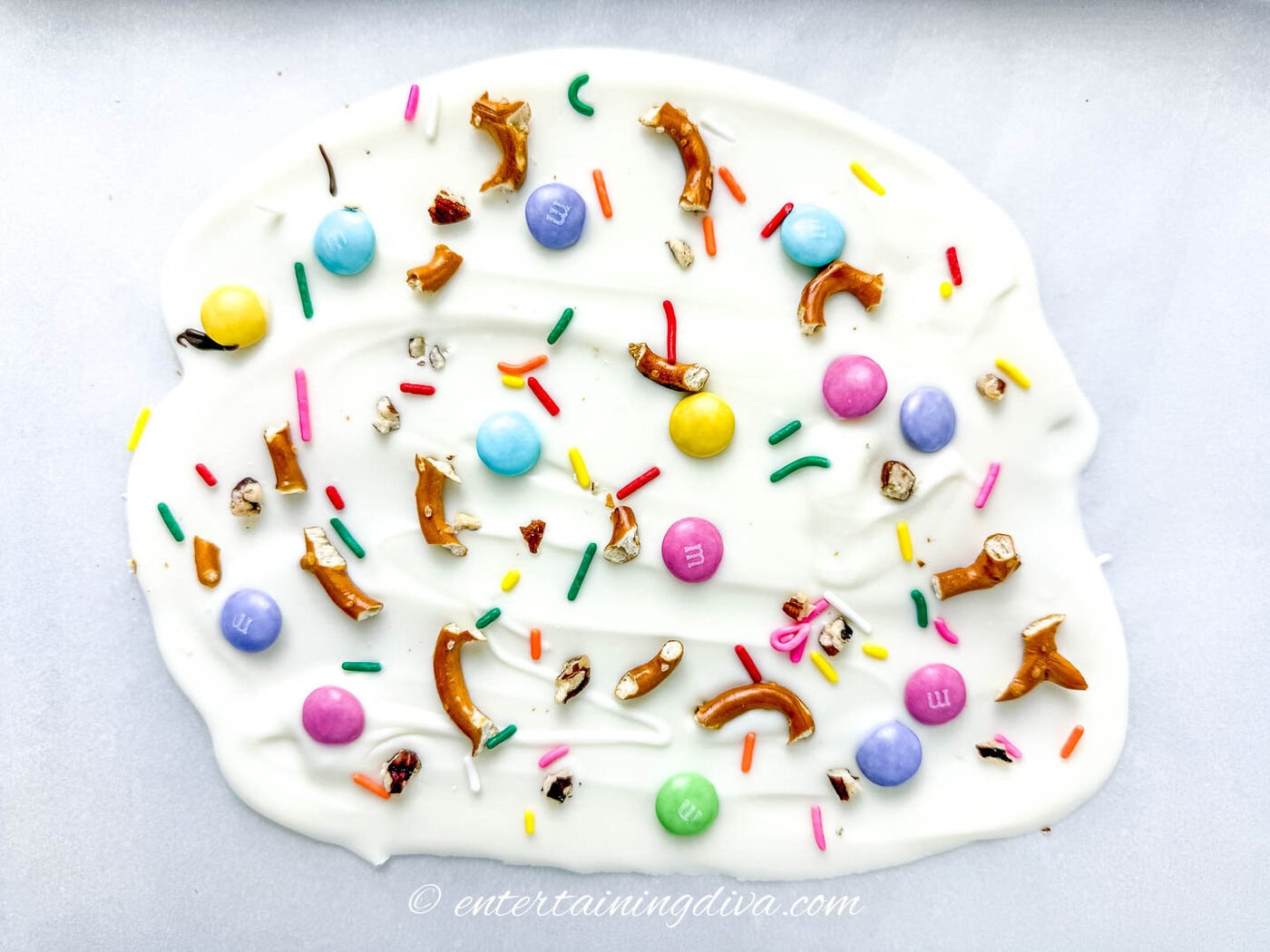 Melted white chocolate topped with M&M's pretzels and sprinkles