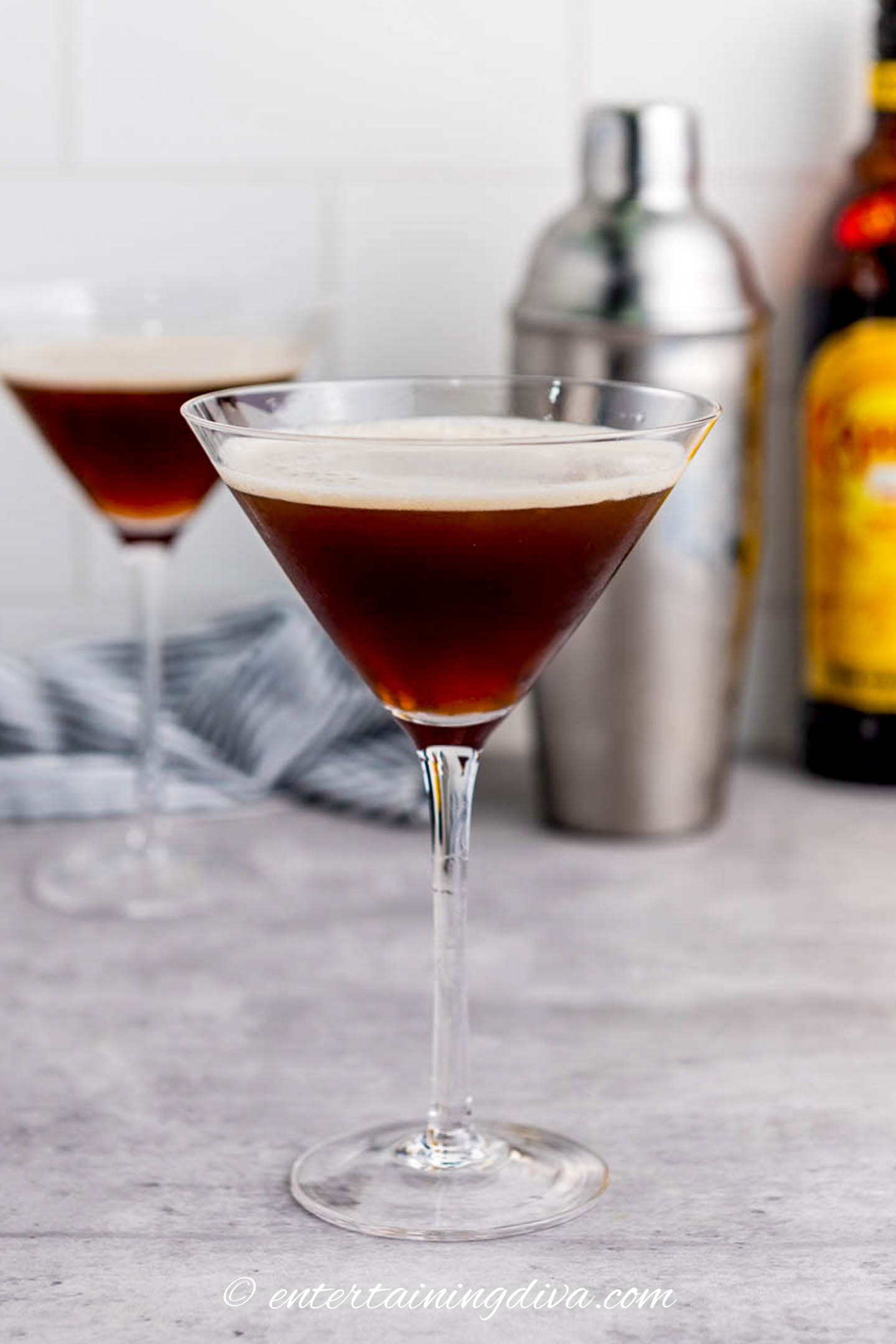 side view of an espresso martini with a cocktail shaker a bottle of Kahlua in the background