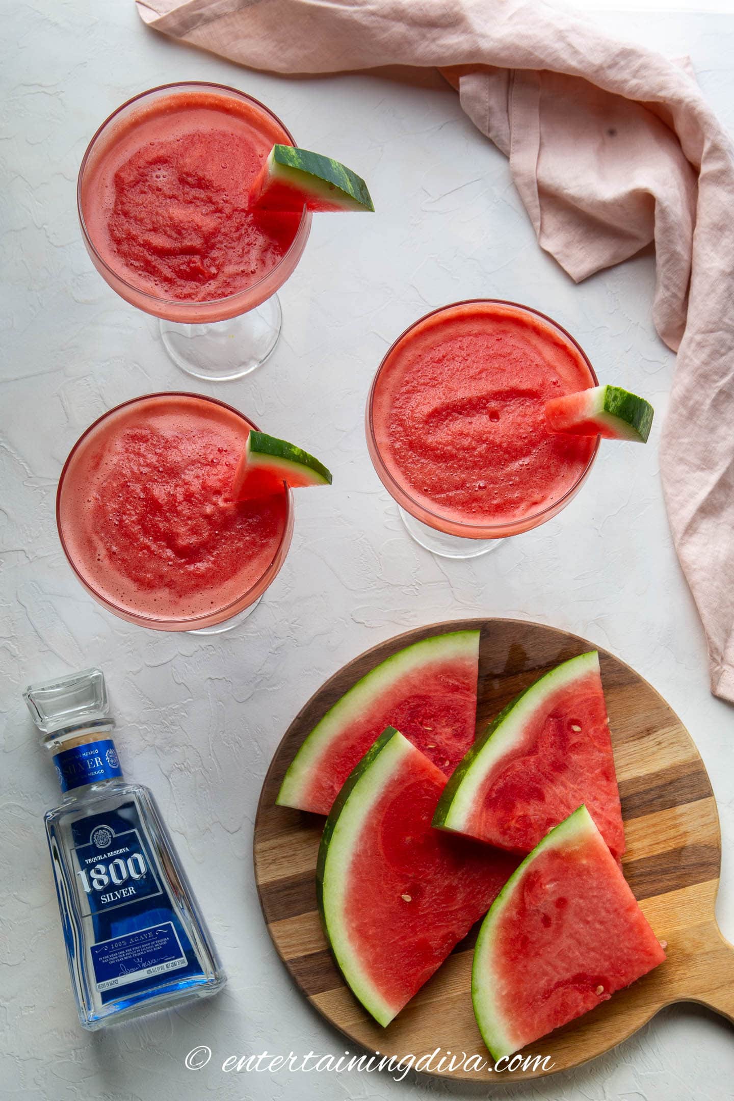 overhead picture of watermelon margaritas with a bottle of tequila and fresh watermelon slices