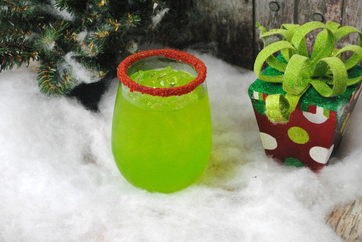 A green drink with a red rim sitting next to a christmas tree.