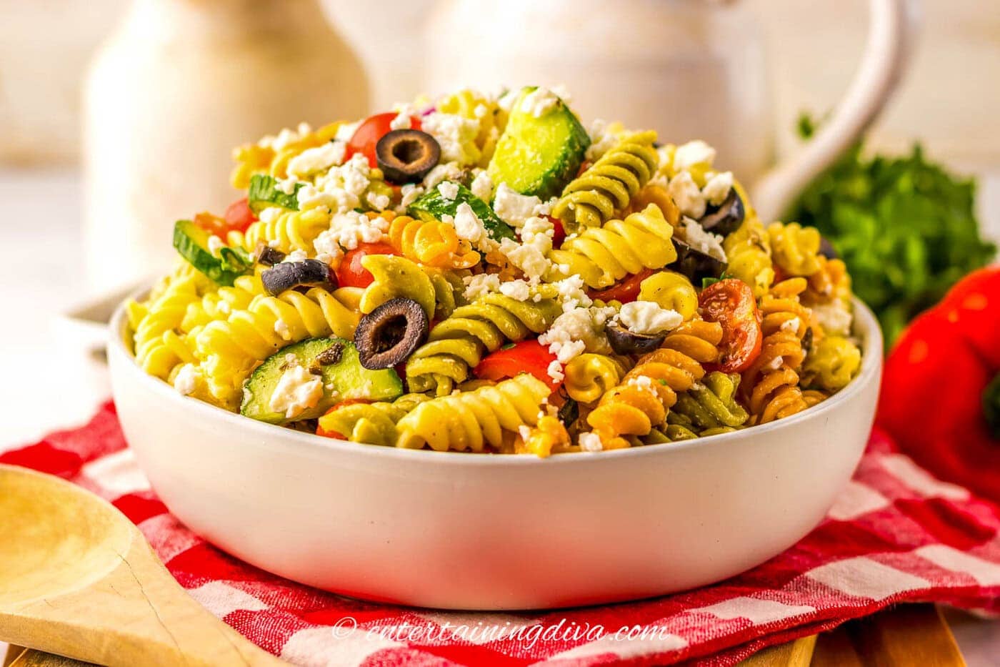 side view of a bowl of greek pasta salad on a red and white checkered napkin
